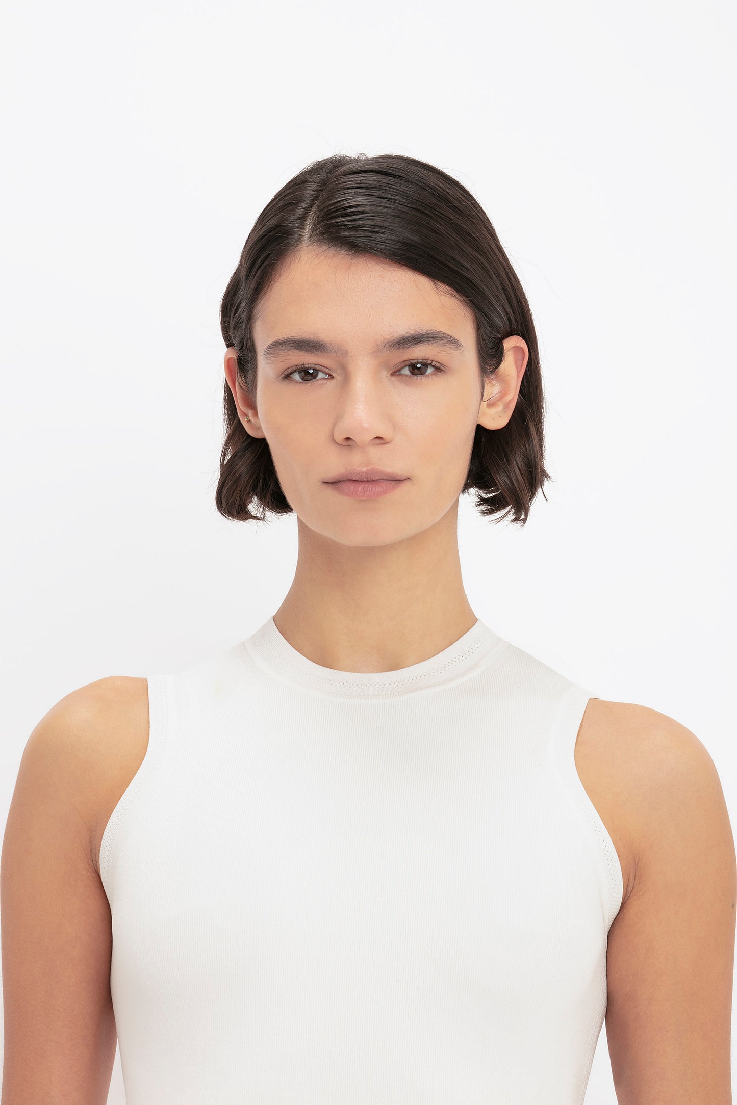 A person with short, dark hair wearing a Victoria Beckham VB Body Mini Dress in white looks directly at the camera against a plain white background.