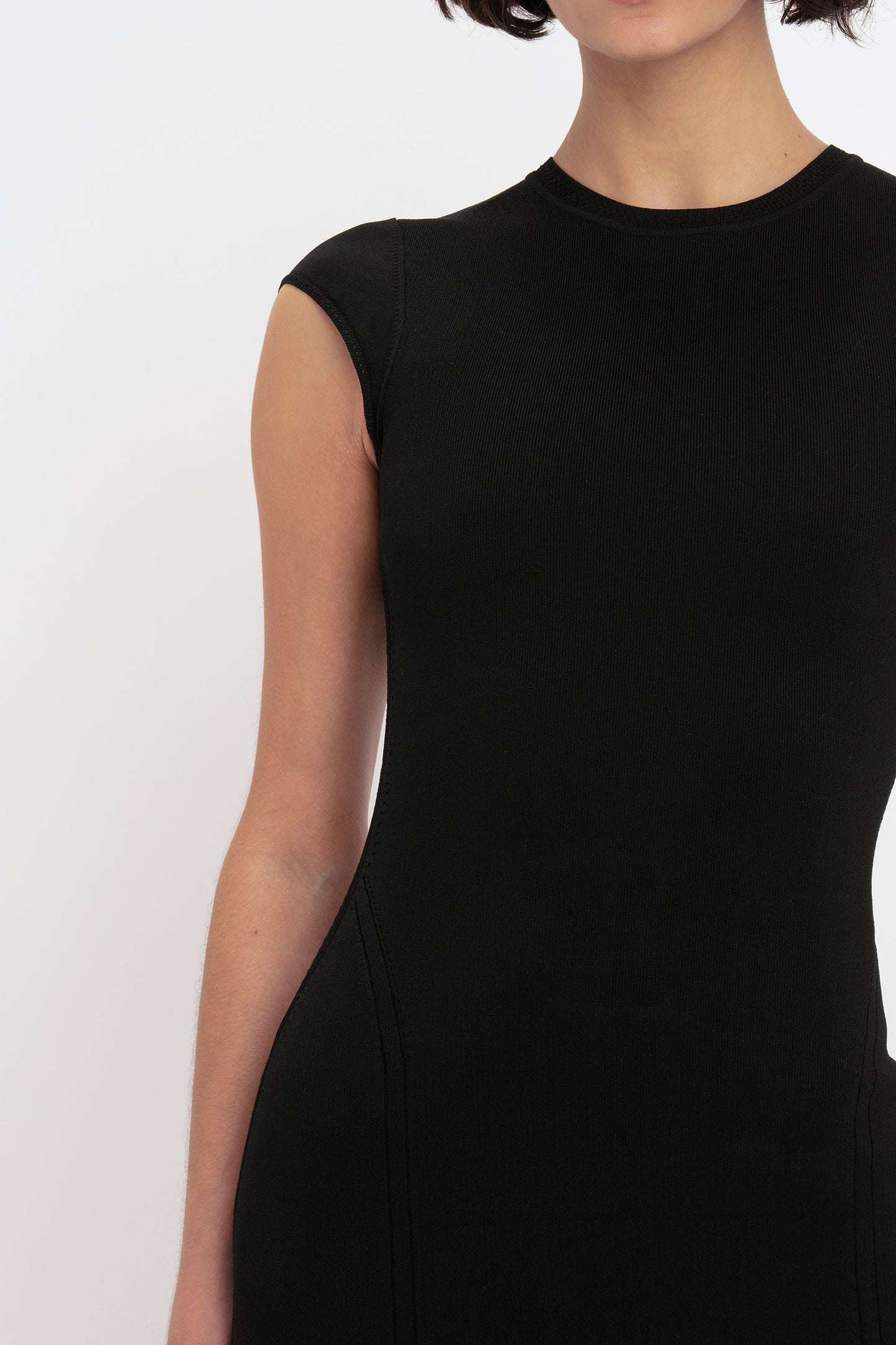 A woman wearing the VB Body Compact Cap Sleeve Mini Dress in Black by Victoria Beckham, shown from shoulders to mid-thigh, stands against a plain white background.