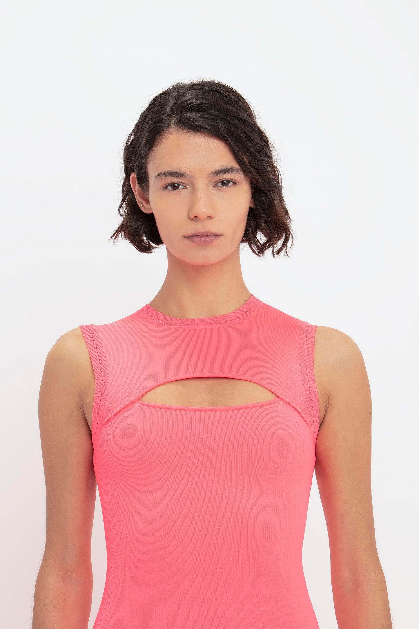 A woman with short dark hair, wearing the VB Body Slash Front Midi Dress in Pink by Victoria Beckham, stands against a plain white background.