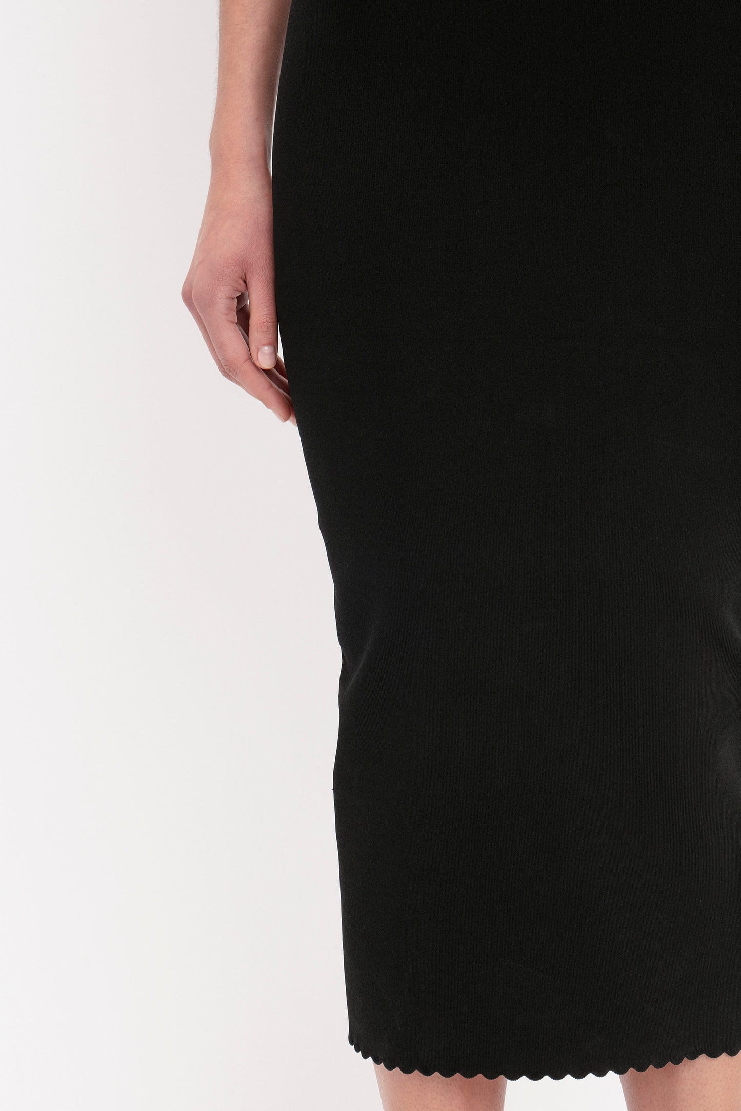A person standing in a Victoria Beckham VB Body Cut Out Midi Dress in Black, showing the lower part of their body and right arm.