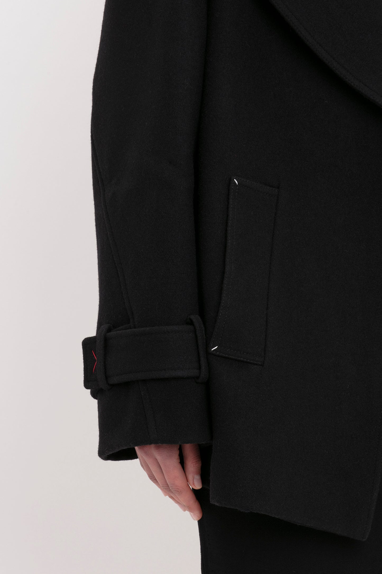 Close-up of a person's left arm wearing the VB Body Cut Out Midi Dress in Black by Victoria Beckham, featuring a belt detail at the wrist and a flap pocket.