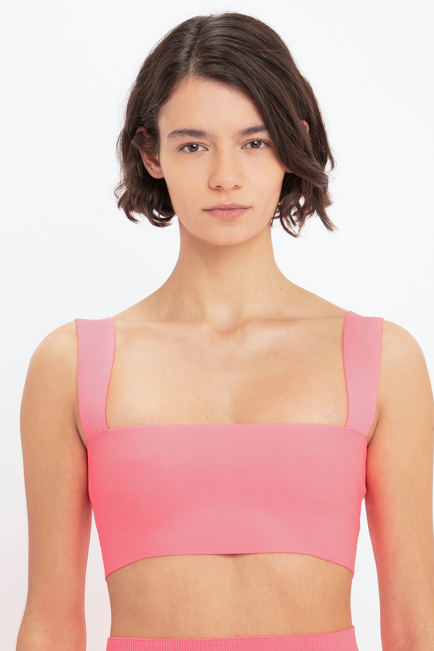 Individual with short dark hair, adorned in a pink VB Body Fitted Midi Skirt from Victoria Beckham, stands against a plain white background.