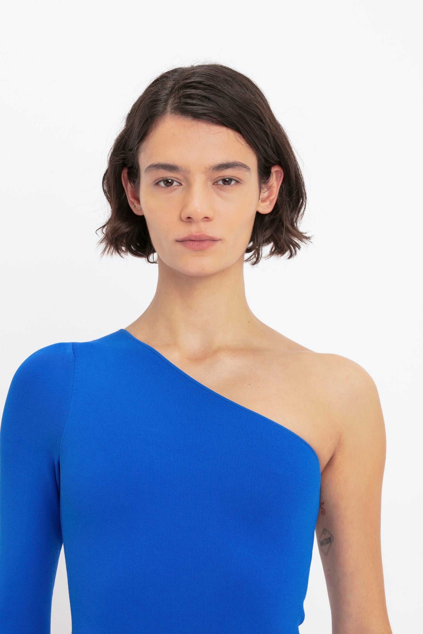 A person with short, dark hair wears the Victoria Beckham VB Body One Shoulder Midi Dress in Cobalt against a plain white background.