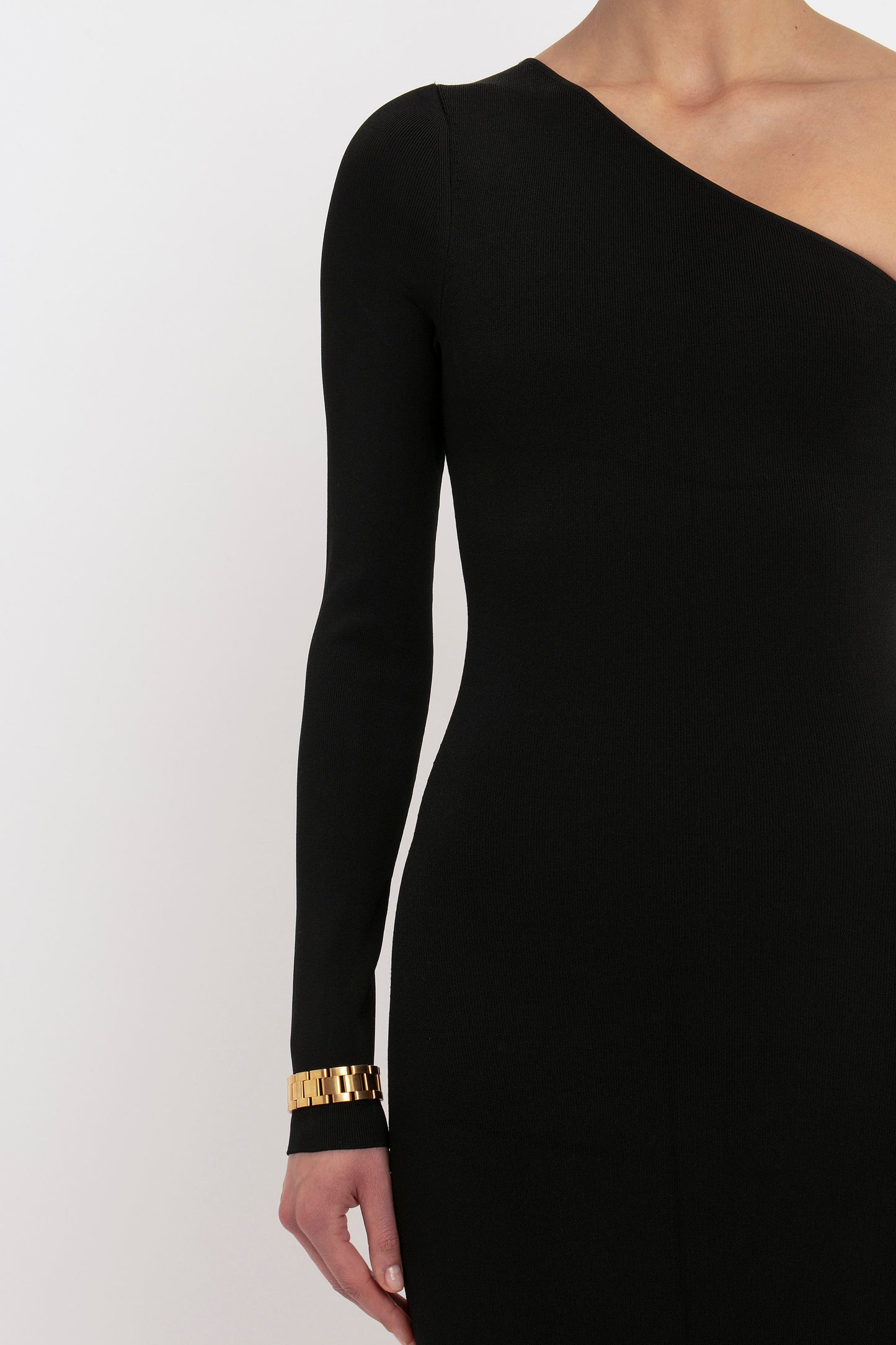 A person is wearing the VB Body One Shoulder Top in Black from Victoria Beckham, paired with a gold bracelet. The image captures the upper body from chest to hip.