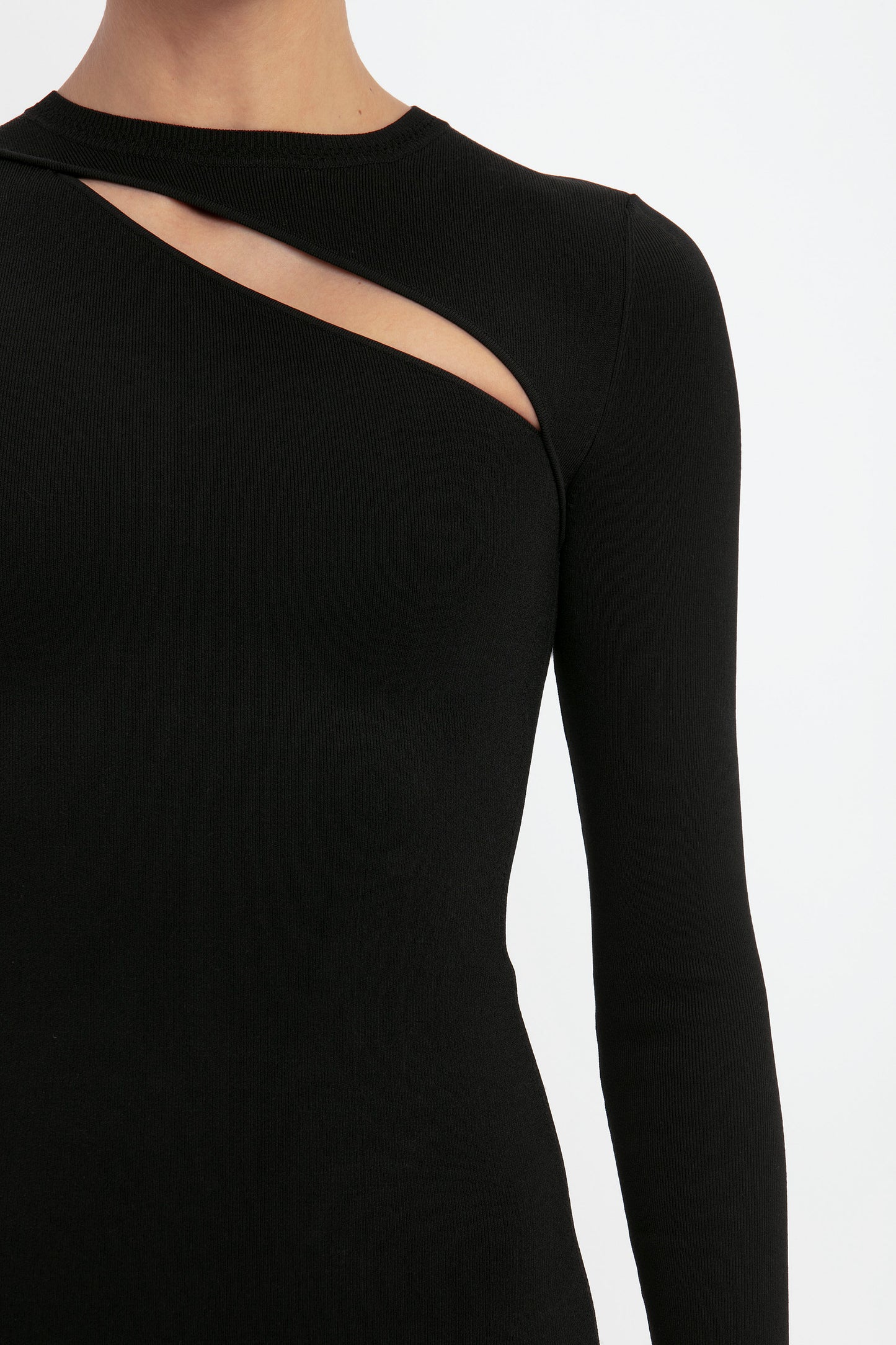 A person wearing the VB Body Front Slash Crew Neck Top in Black by Victoria Beckham, featuring a long-sleeve design with an asymmetrical cutout across the upper chest and shoulder.