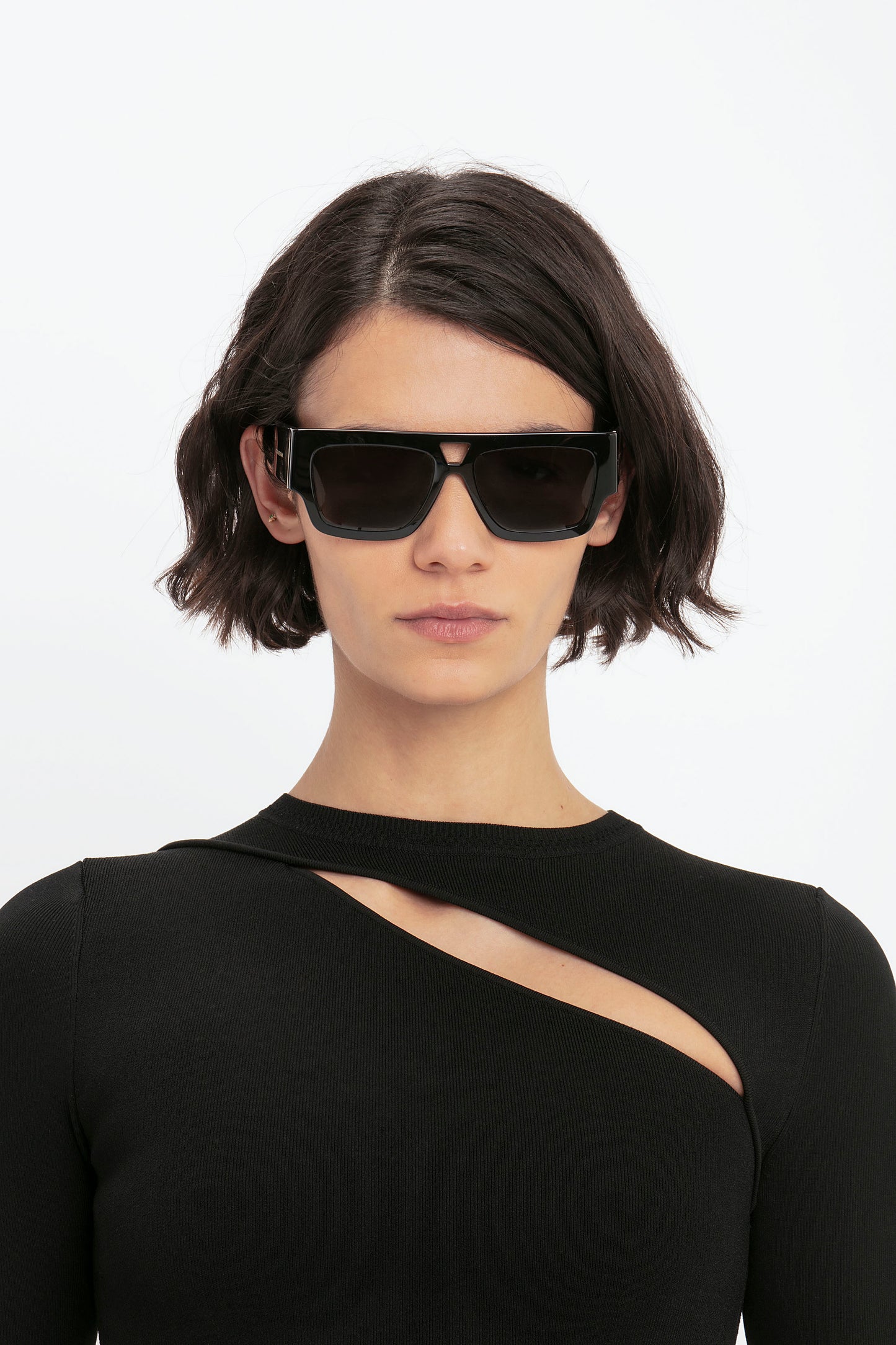 Individual with short, dark hair wearing black sunglasses and a black VB Body Front Slash Crew Neck Top by Victoria Beckham.