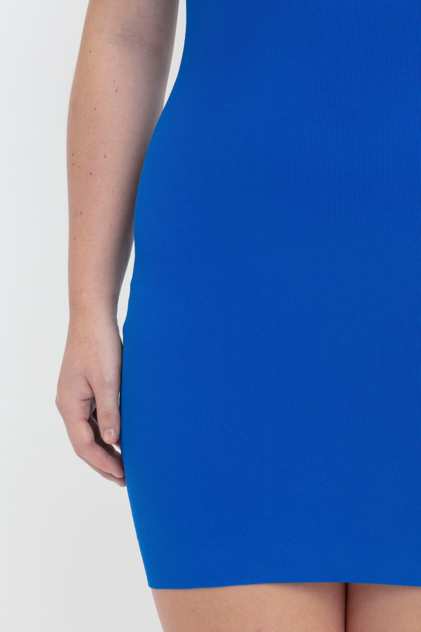 A person wearing the VB Body Mini Dress in Cobalt by Victoria Beckham, with their left arm resting at their side. The image captures the midsection down to the thighs.