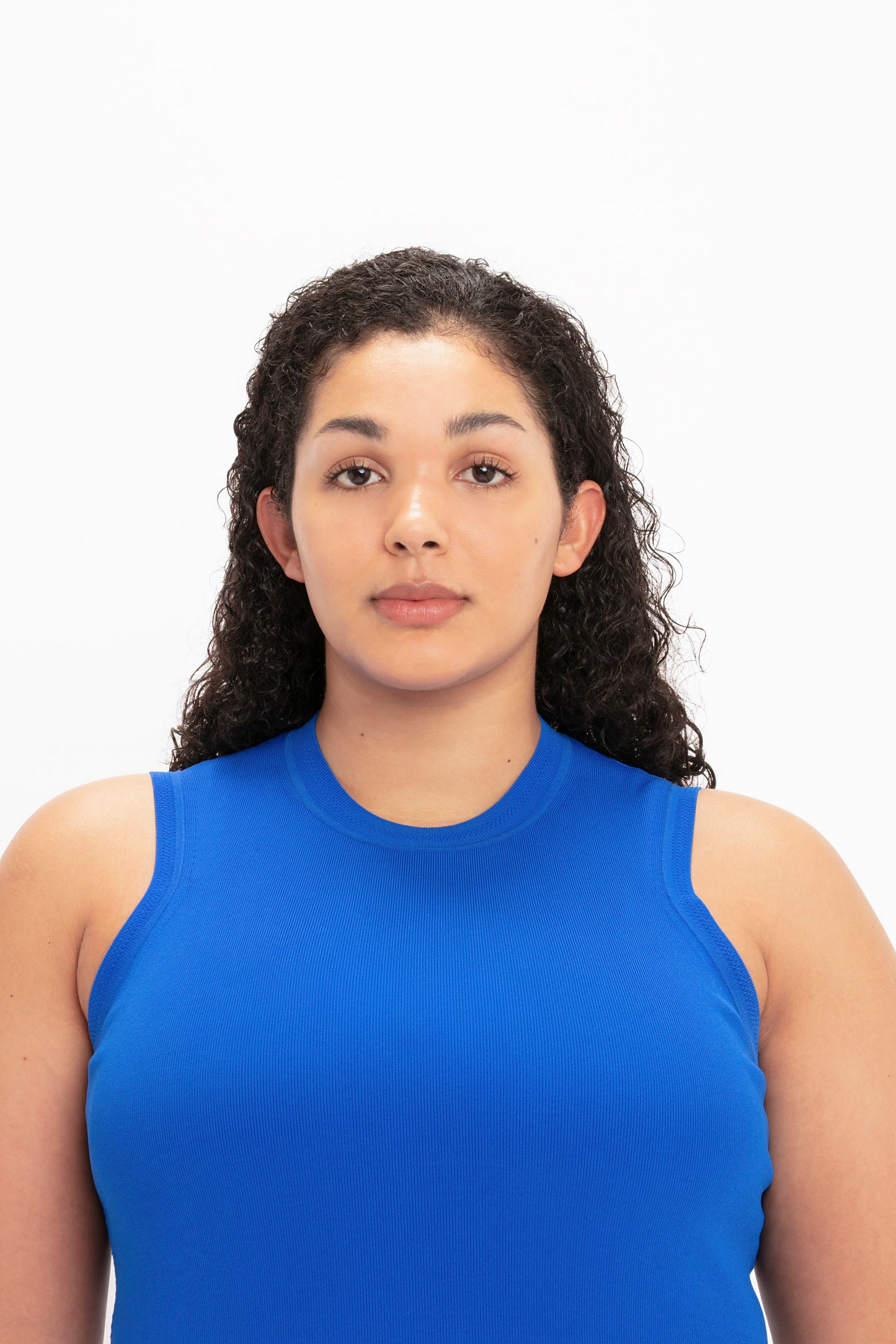 A person with curly hair wearing the VB Body Mini Dress in Cobalt by Victoria Beckham faces the camera against a plain white background.