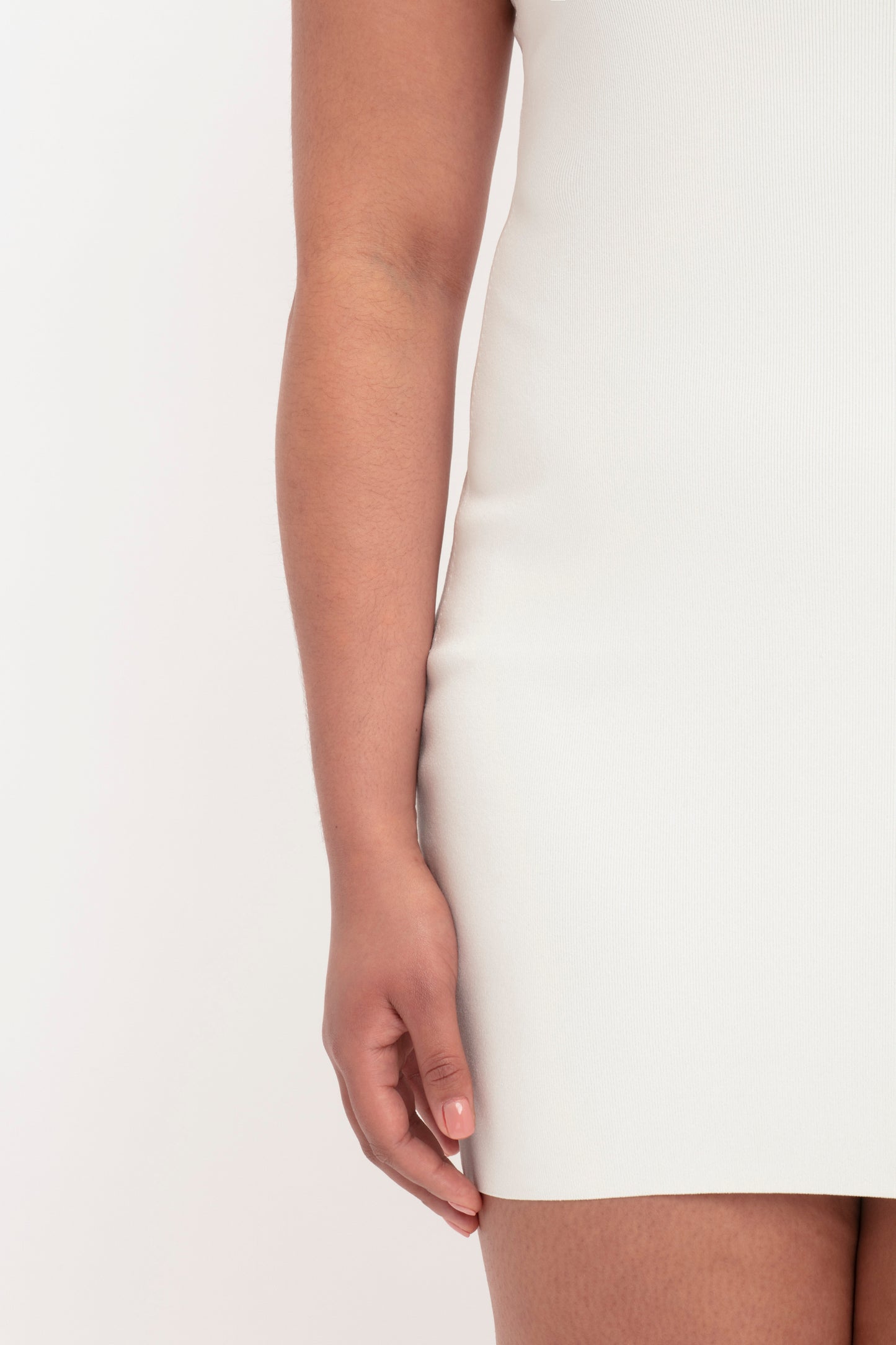 Close-up of a person's left arm and hand resting against their body, standing in the Victoria Beckham VB Body Mini Dress in White.