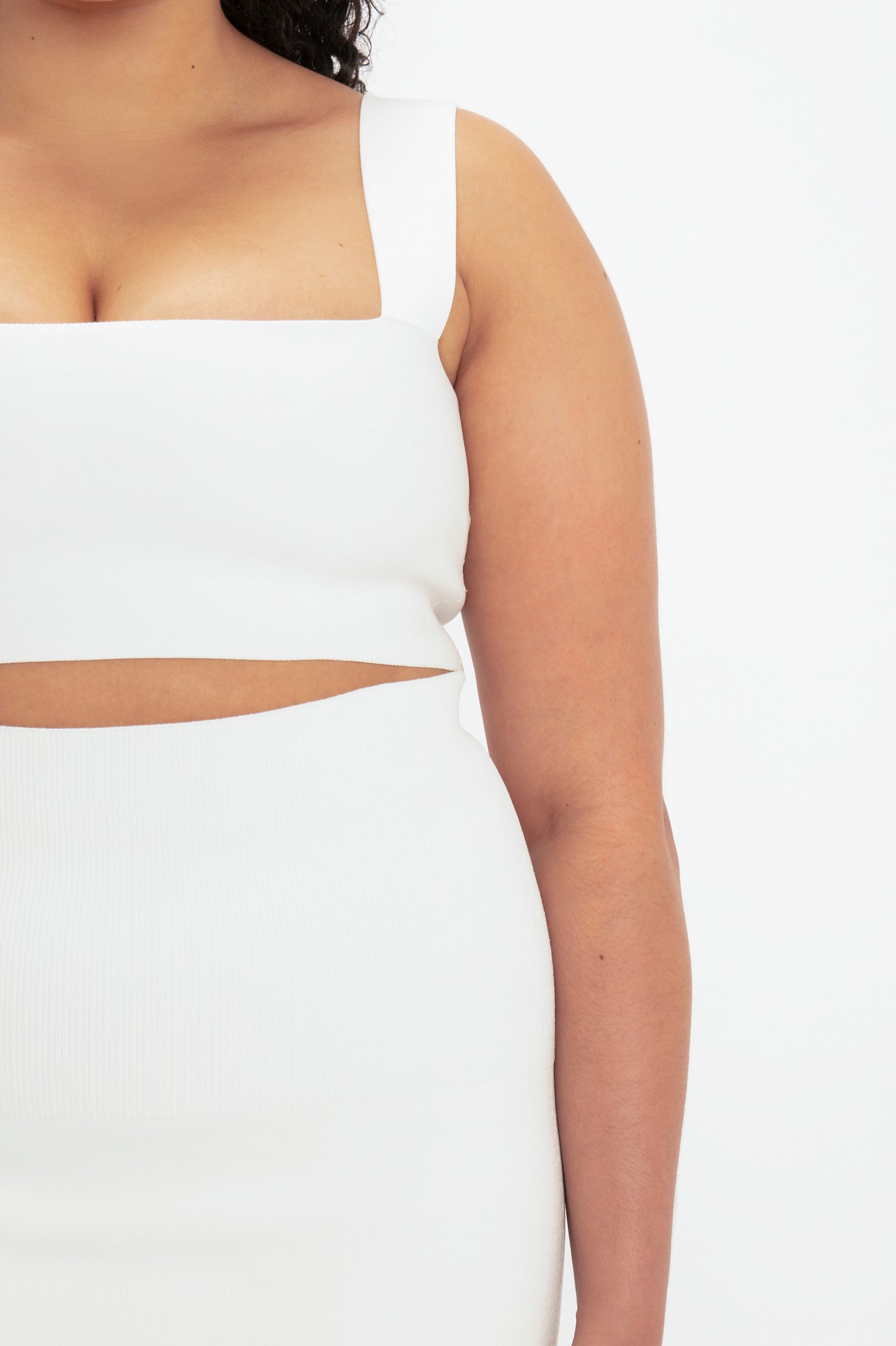 Close-up of a person wearing the VB Body Strap Bandeau Top in White by Victoria Beckham, paired with a white high-waisted bottom featuring a cutout section between the two pieces.