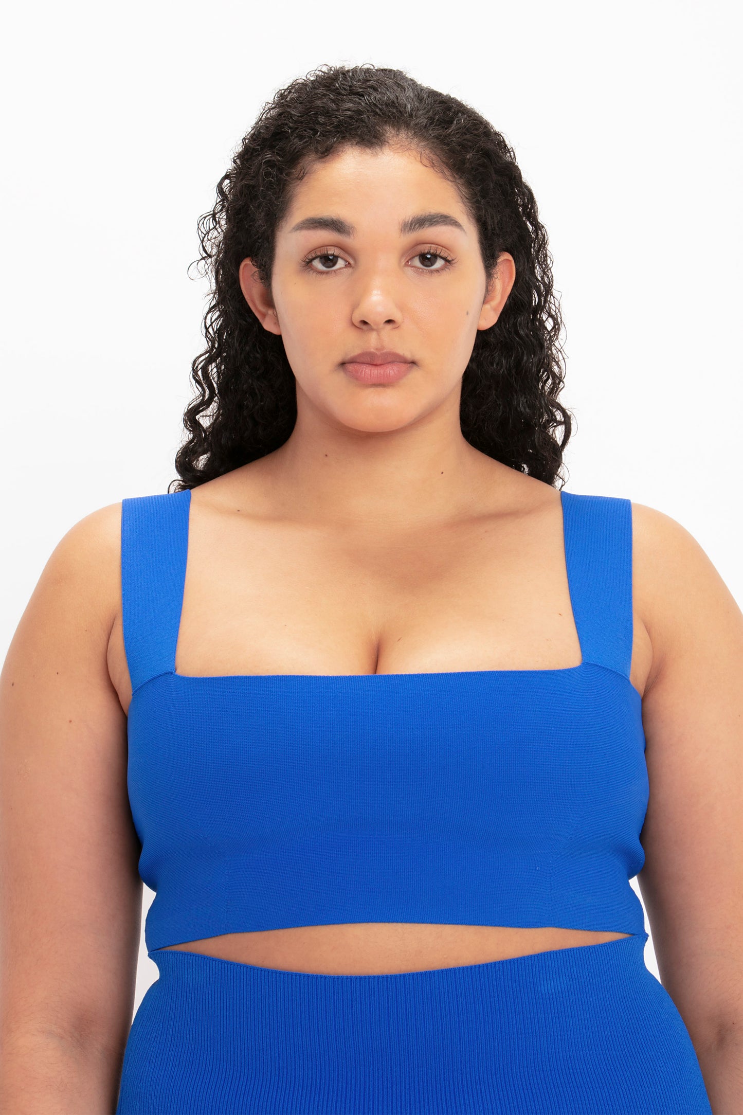 A person with curly black hair is wearing a VB Body Strap Bandeau Top in Colbalt by Victoria Beckham, facing the camera against a plain background.