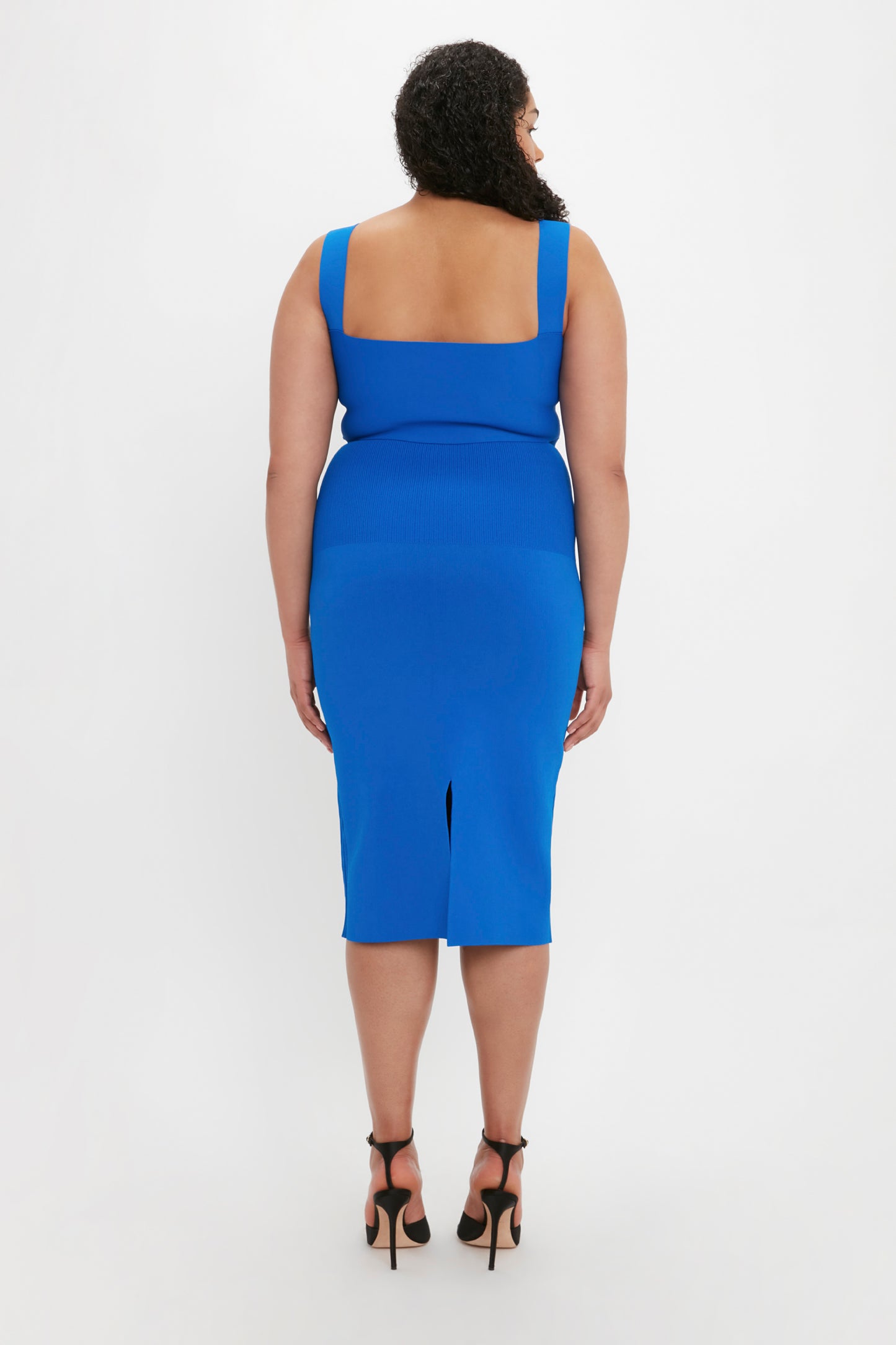 A person with curly hair wearing the VB Body Strap Bandeau Top in Cobalt by Victoria Beckham stands facing away from the camera on a white background.