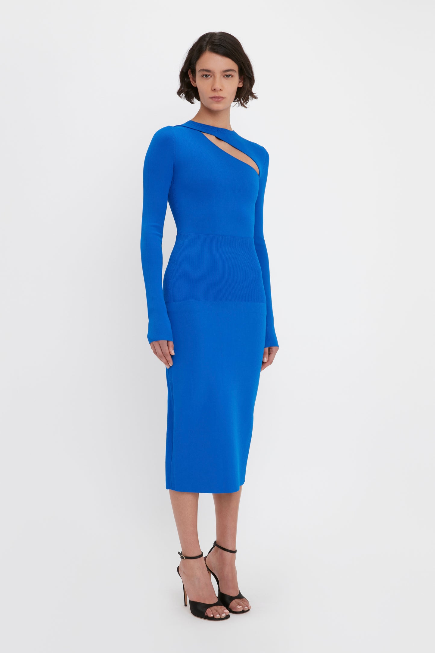 A person stands against a plain background wearing the VB Body Front Slash Crew Neck Top in Cobalt by Victoria Beckham, paired with black high-heeled shoes.