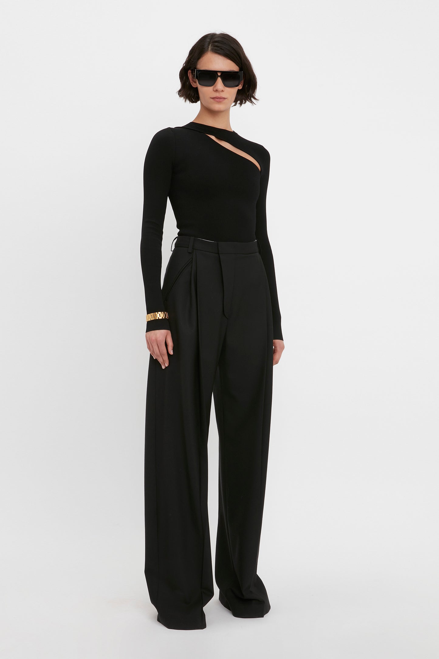 Person wearing the Victoria Beckham VB Body Front Slash Crew Neck Top in Black and wide-leg trousers, accessorized with sunglasses and a bracelet.