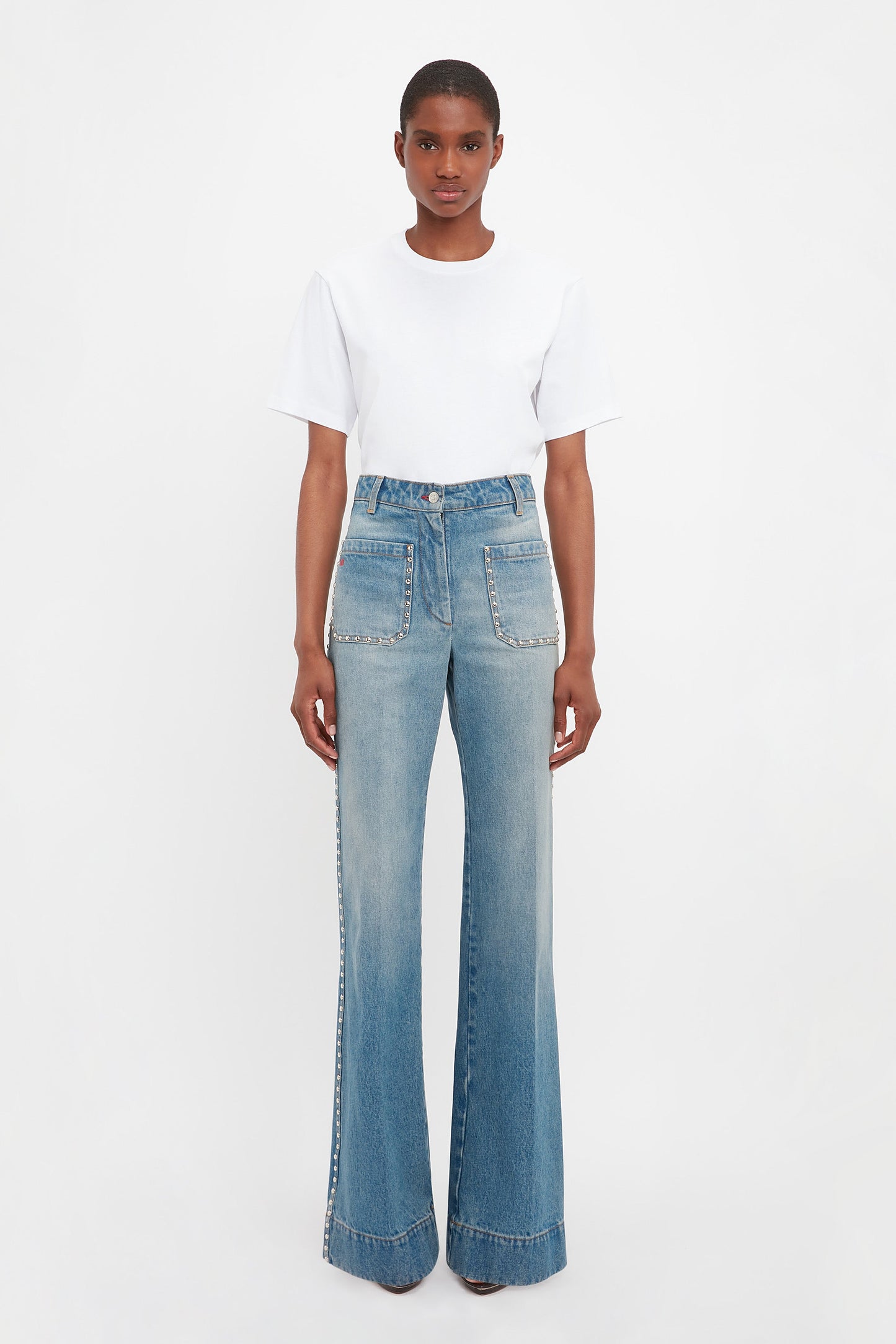 Someone stands facing forward, wearing a white t-shirt and Victoria Beckham's BAO TEST R - Alina High Waisted Jeans in Vintage Wash with front patch pockets.