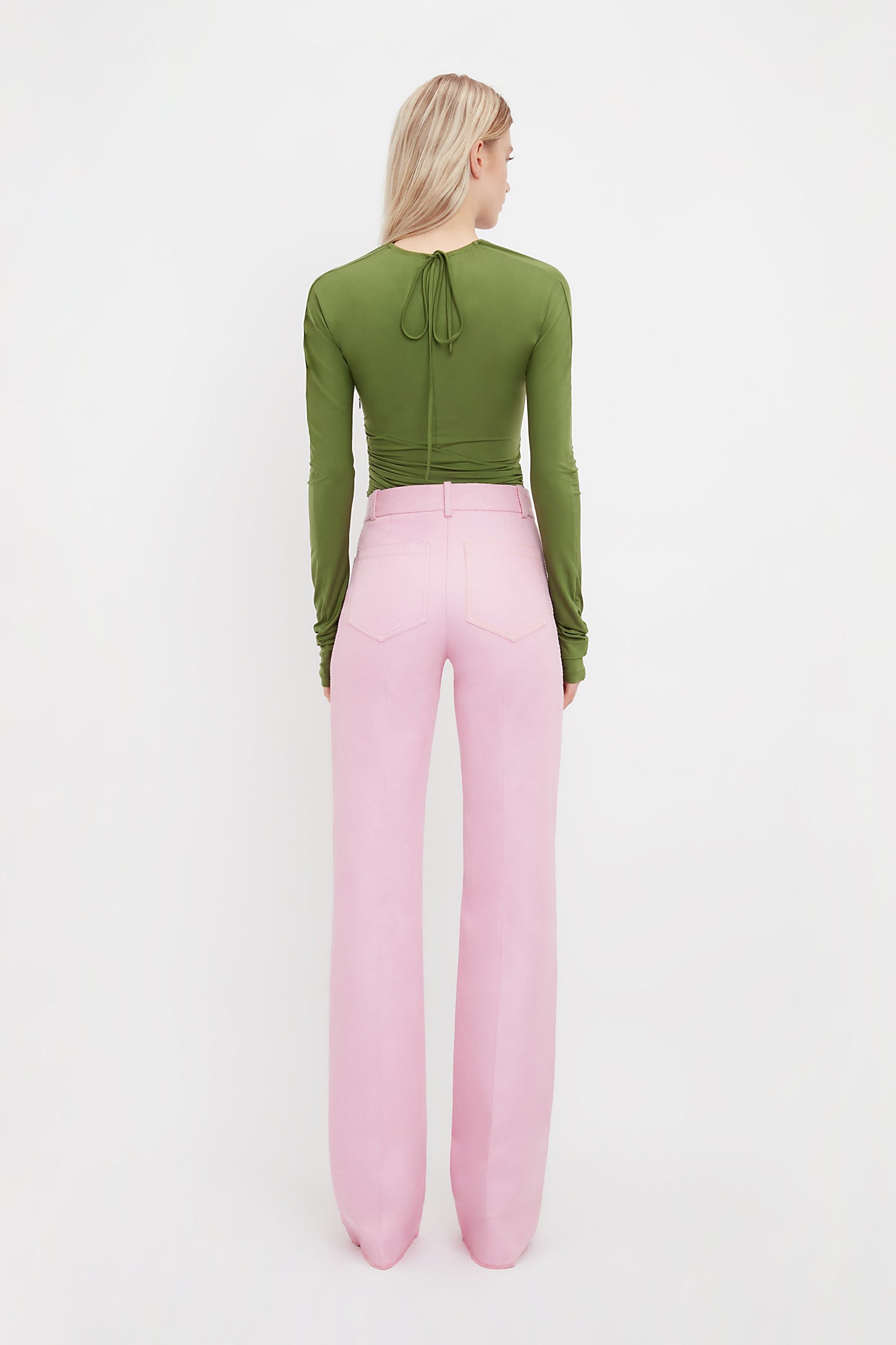 A person faces away in a fitted green long-sleeve top and high-waisted Alina Tailored Trouser In Bubblegum by Victoria Beckham, channeling a chic 70s silhouette against a plain white background.