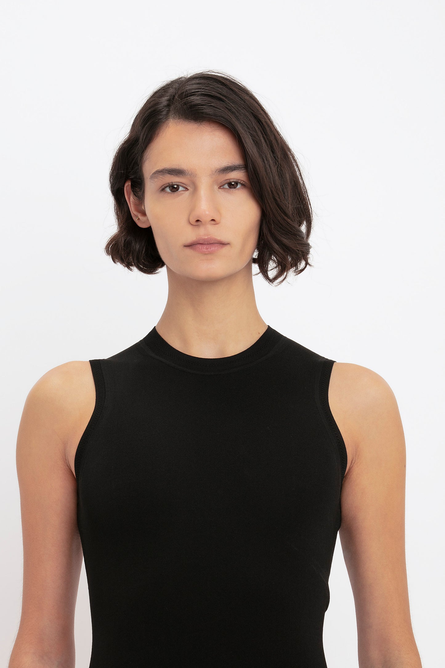 A person with short, dark hair wearing the VB Body Mini Dress in Black by Victoria Beckham is facing the camera against a plain white background.