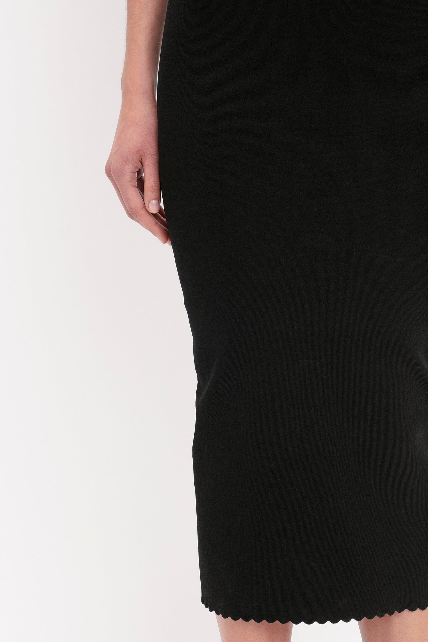 A person standing in a Victoria Beckham VB Body Cut Out Midi Dress in Black, showing the lower part of their body and right arm.
