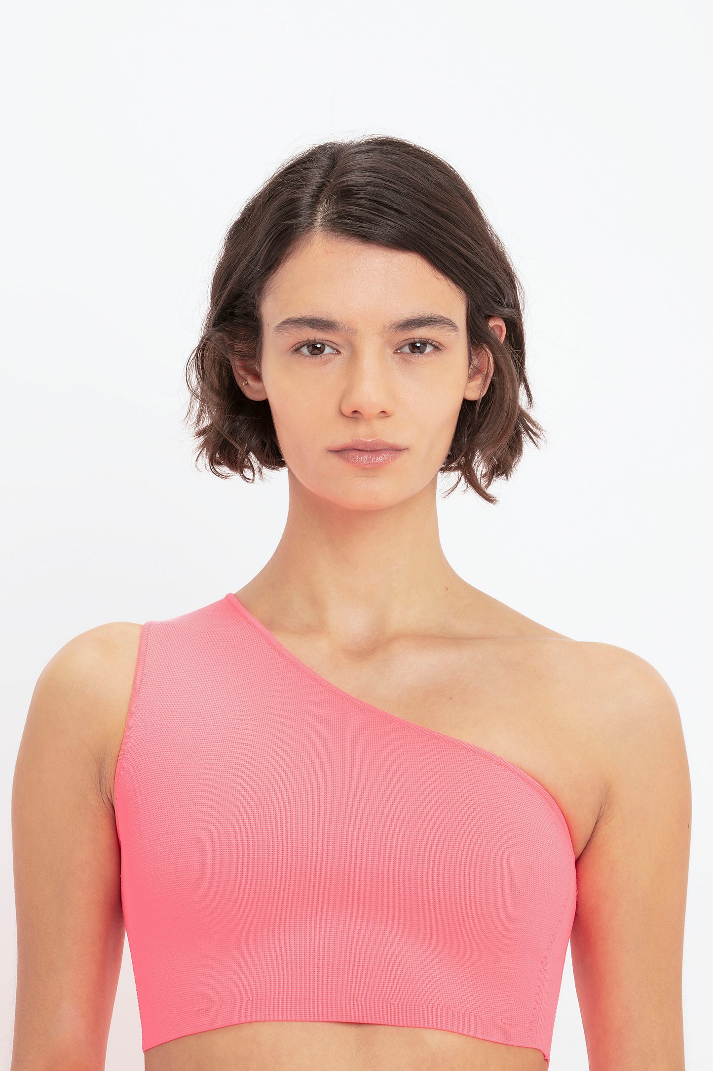 A person wearing the VB Body One Shoulder Crop Top in Pink by Victoria Beckham, looking straight at the camera, against a white background.