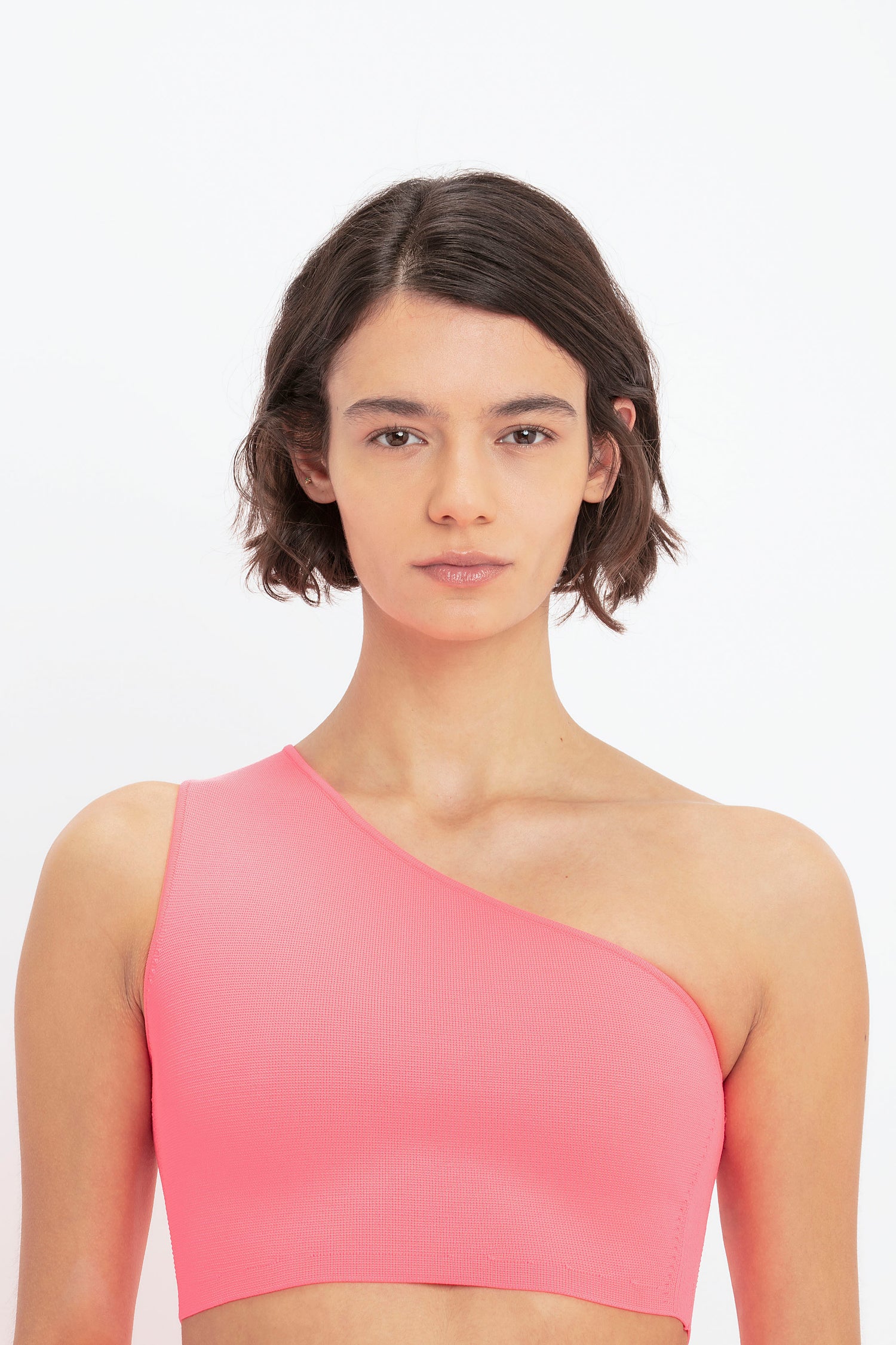 A person wearing the VB Body One Shoulder Crop Top in Pink by Victoria Beckham, looking straight at the camera, against a white background.