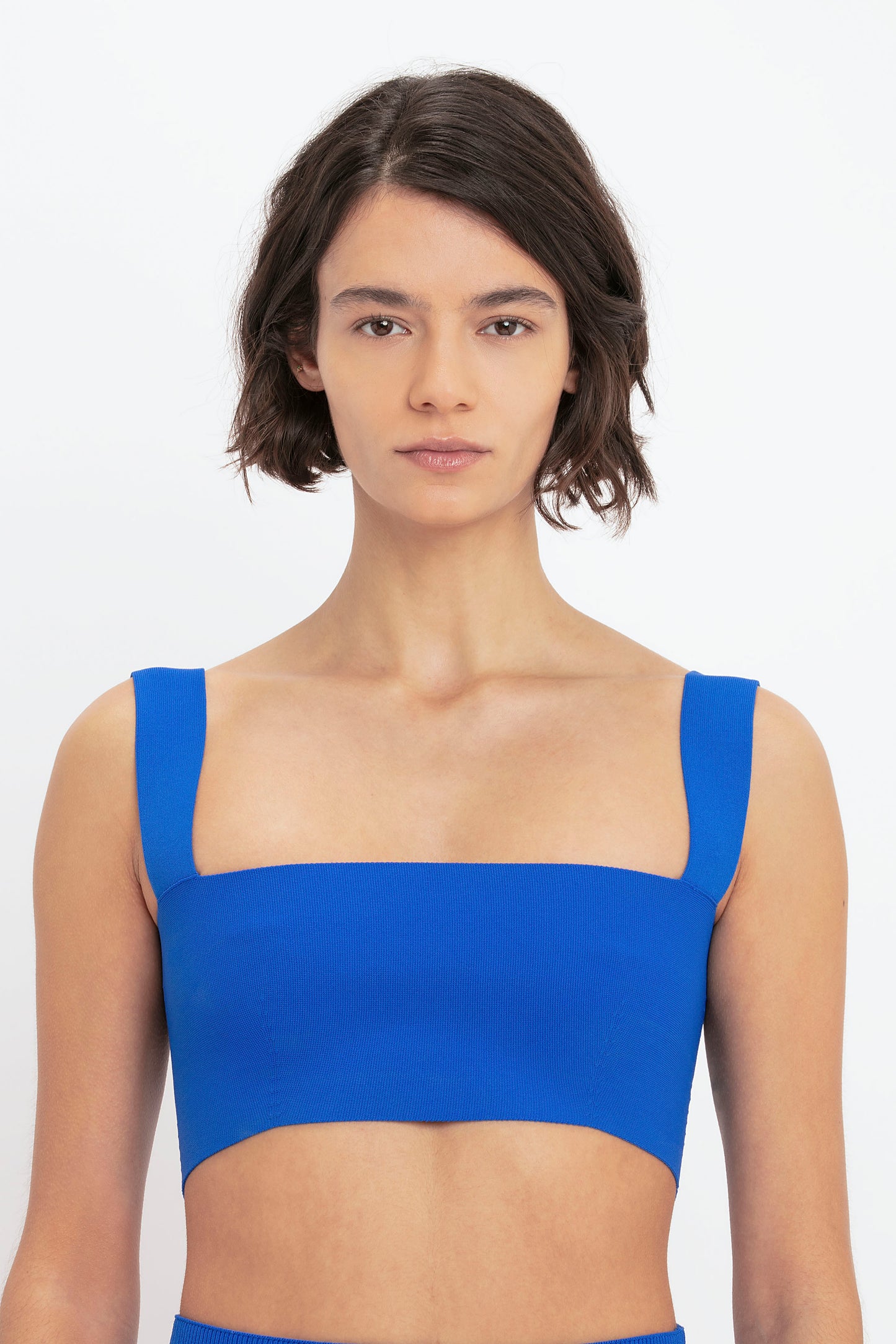 A woman with short brown hair wearing a Victoria Beckham VB Body Strap Bandeau Top in Colbalt stares directly at the camera against a plain white background.