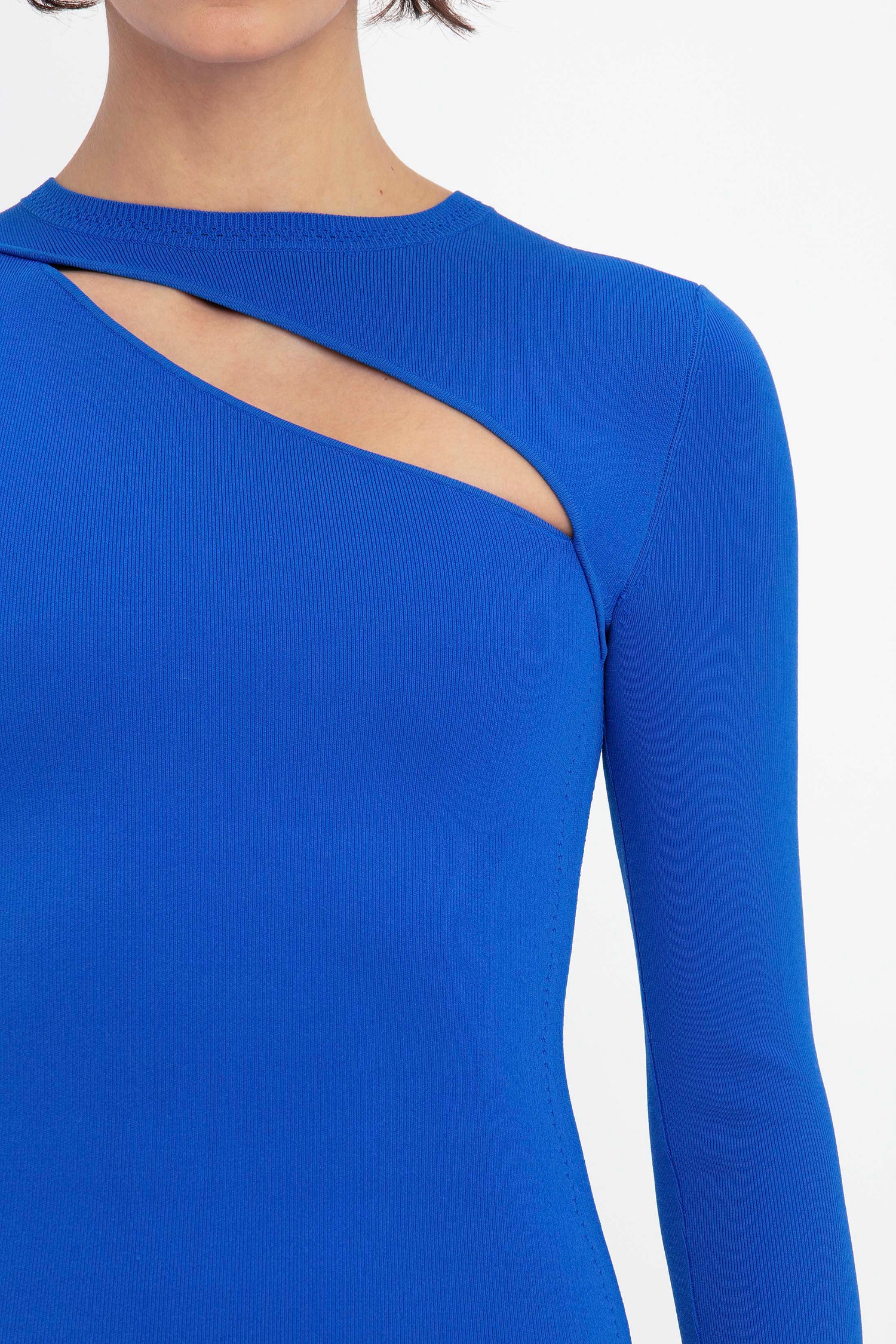 Close-up of a person wearing the VB Body Front Slash Crew Neck Top in Cobalt by Victoria Beckham, featuring a long-sleeve design with an asymmetrical cutout near the neckline.