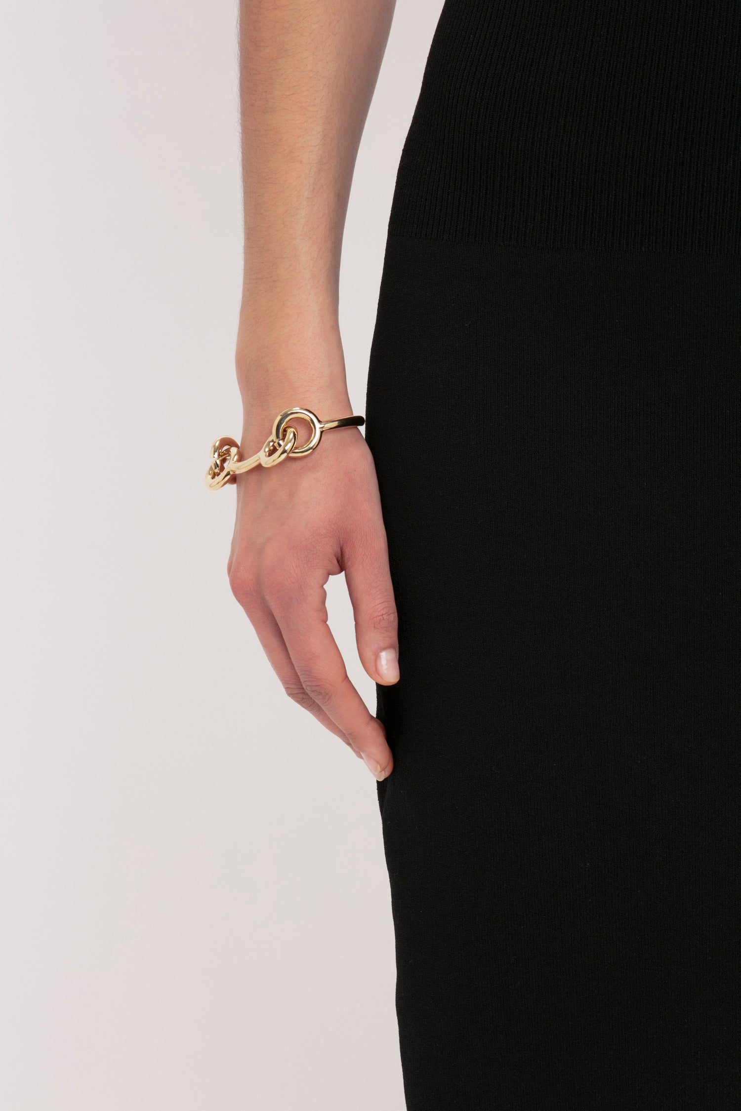 A person wearing the VB Body Fitted Midi Skirt in Black by Victoria Beckham with their hand resting by their side showcasing a gold bracelet.