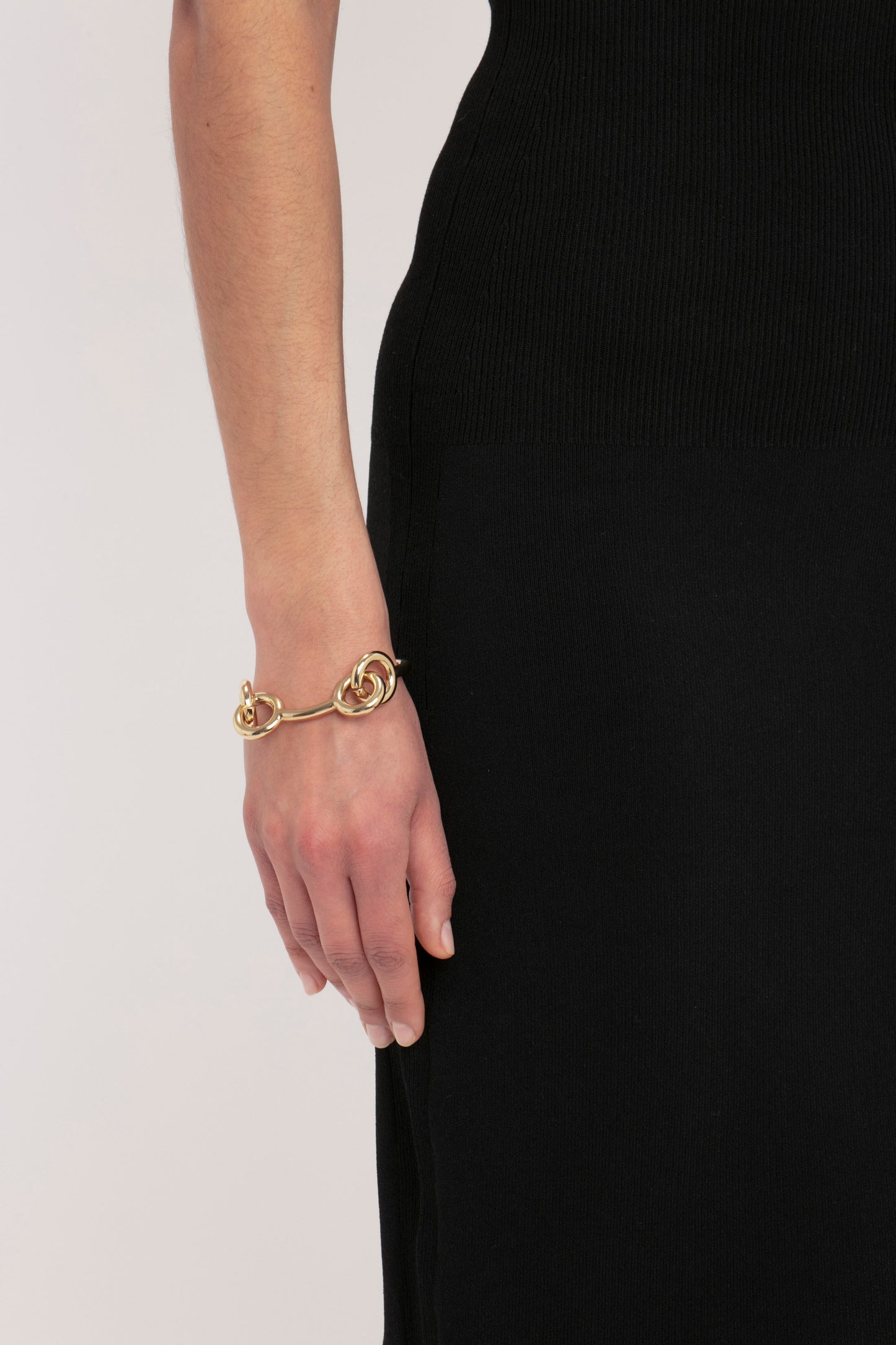 Close-up of a person wearing the Victoria Beckham VB Body Fitted Midi Skirt in Black, with a gold bracelet on their left wrist. Their hand is relaxed and rests at their side.