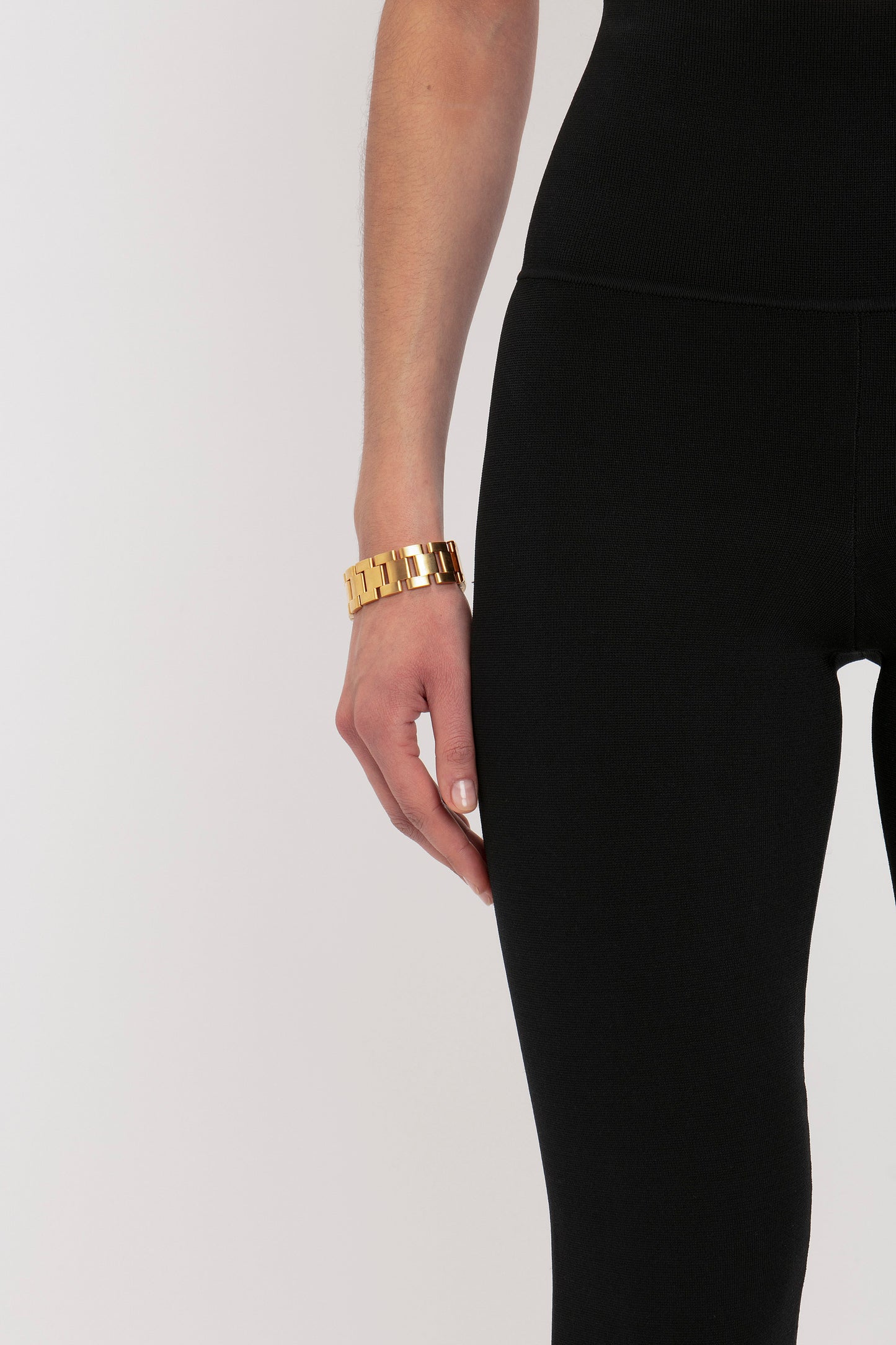 Close-up of a person's arm wearing VB Body Split Front Leggings in Black by Victoria Beckham and a gold bracelet.