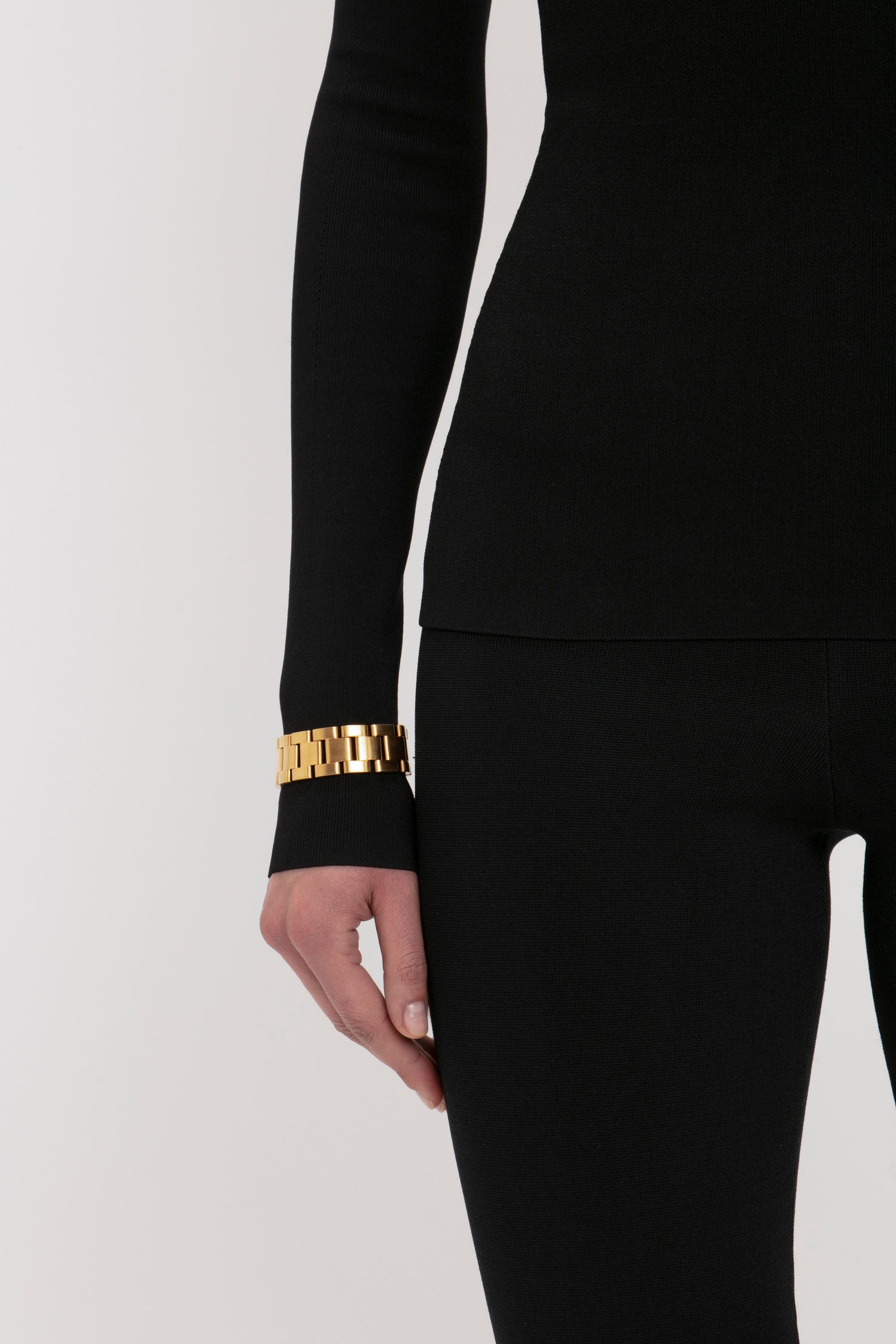 Person wearing a VB Body Front Slash Crew Neck Top in Black by Victoria Beckham and black pants, with a gold link bracelet on their wrist.