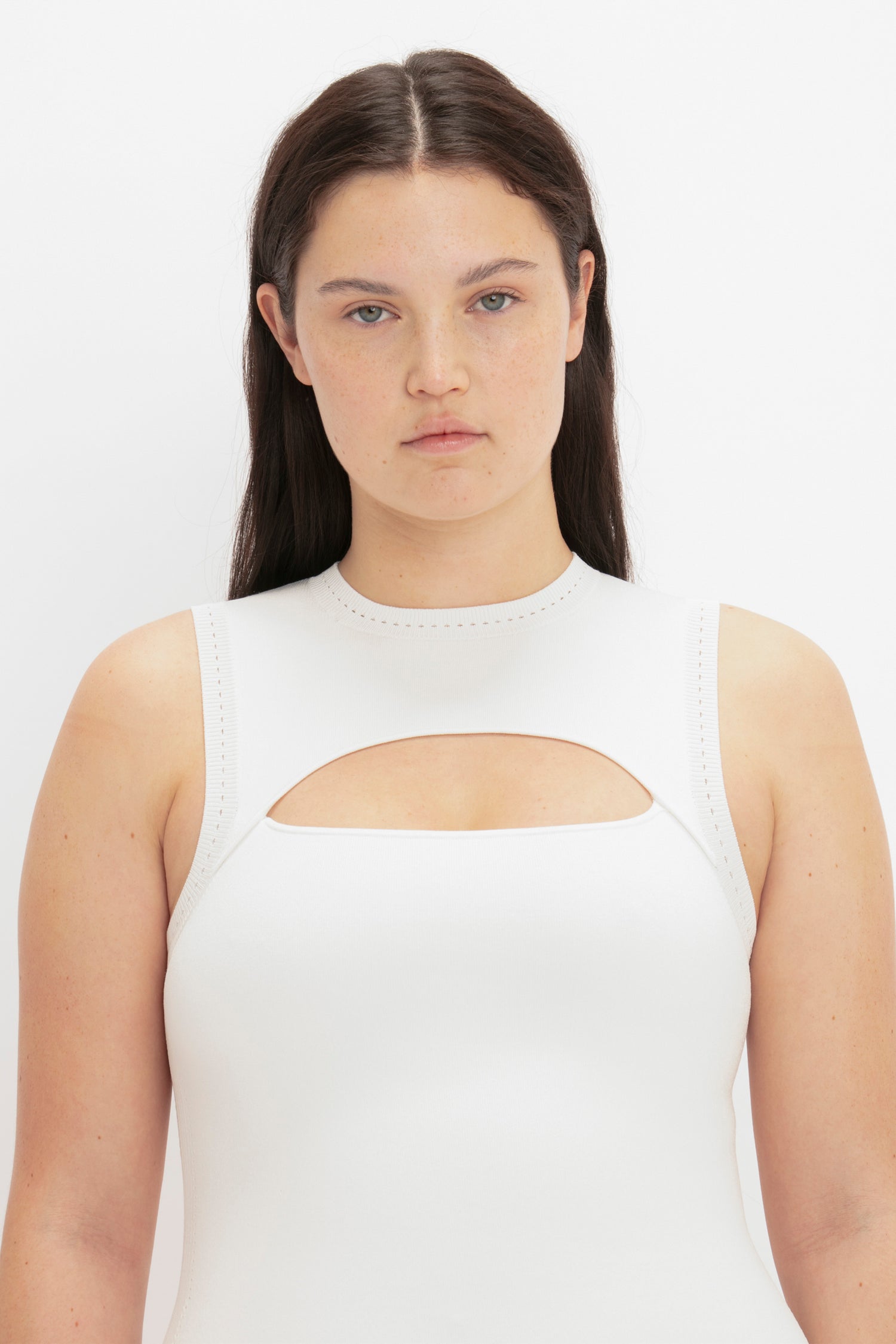 A person with long brown hair is wearing a VB Body Slash Front Midi Dress in White by Victoria Beckham. They are gazing directly at the camera against a plain background.