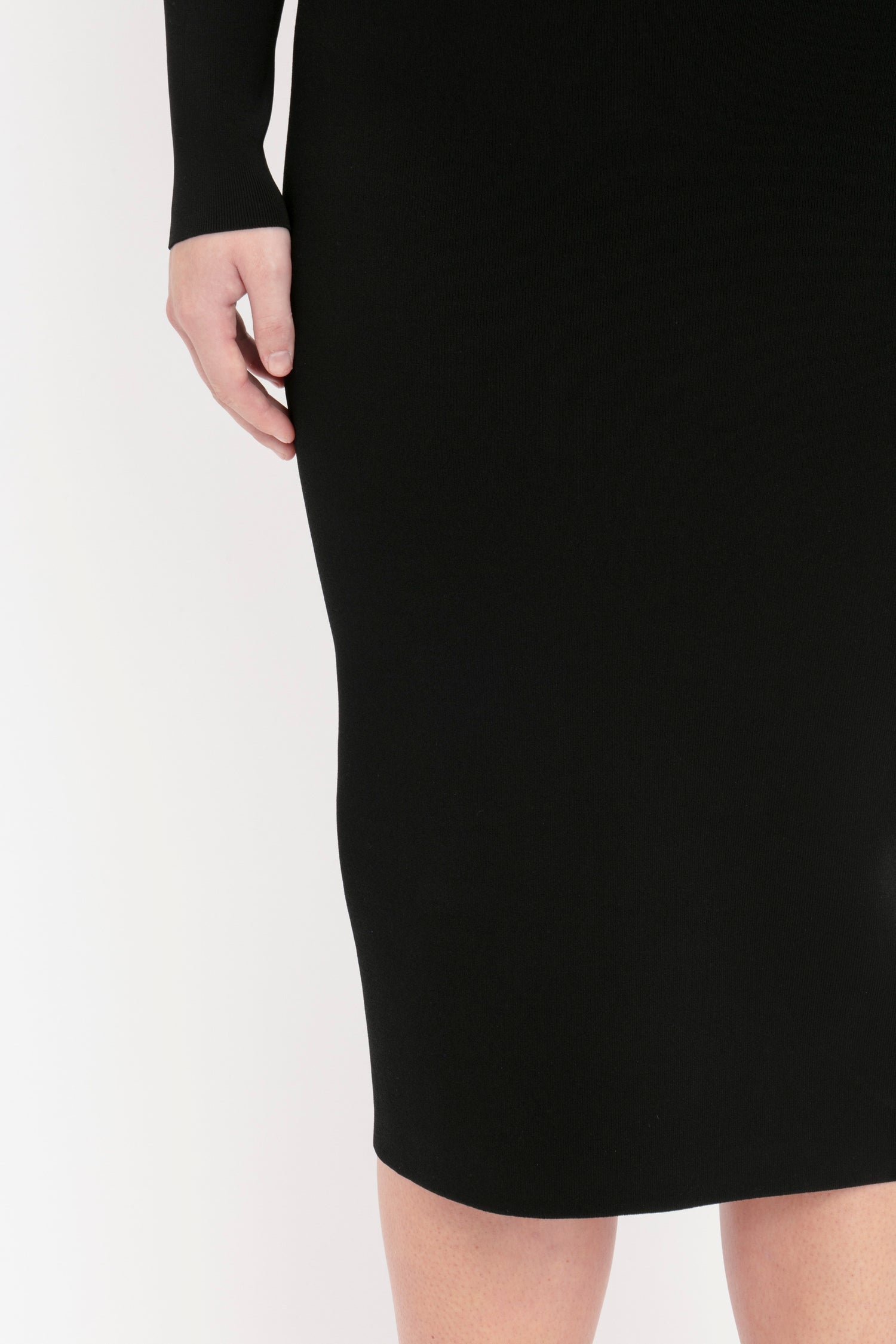 A close-up view of a person wearing the Victoria Beckham VB Body One Shoulder Midi Dress in Black. The person's hand and part of their leg are visible.