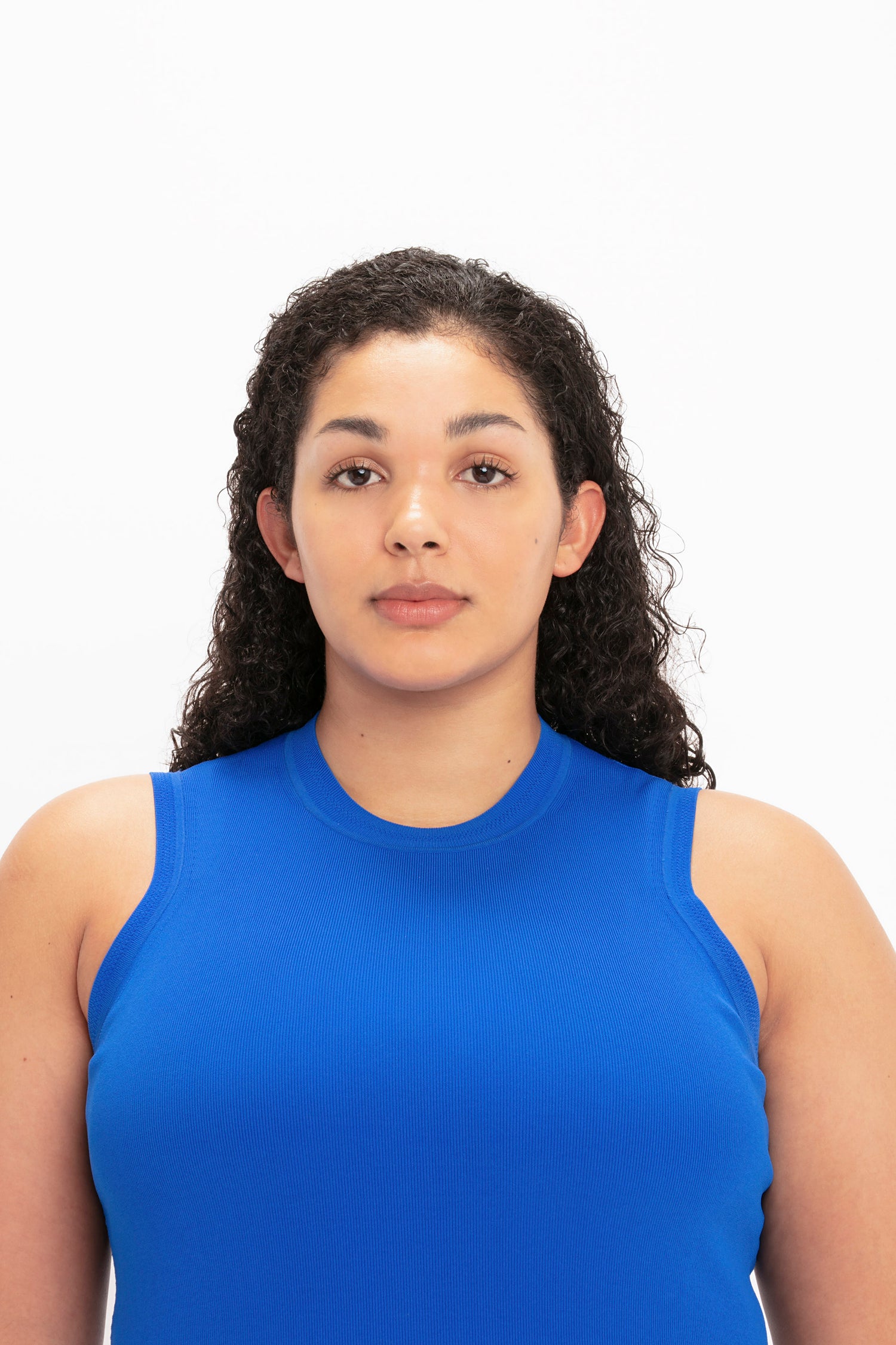 A person with curly hair wearing the VB Body Mini Dress in Cobalt by Victoria Beckham faces the camera against a plain white background.