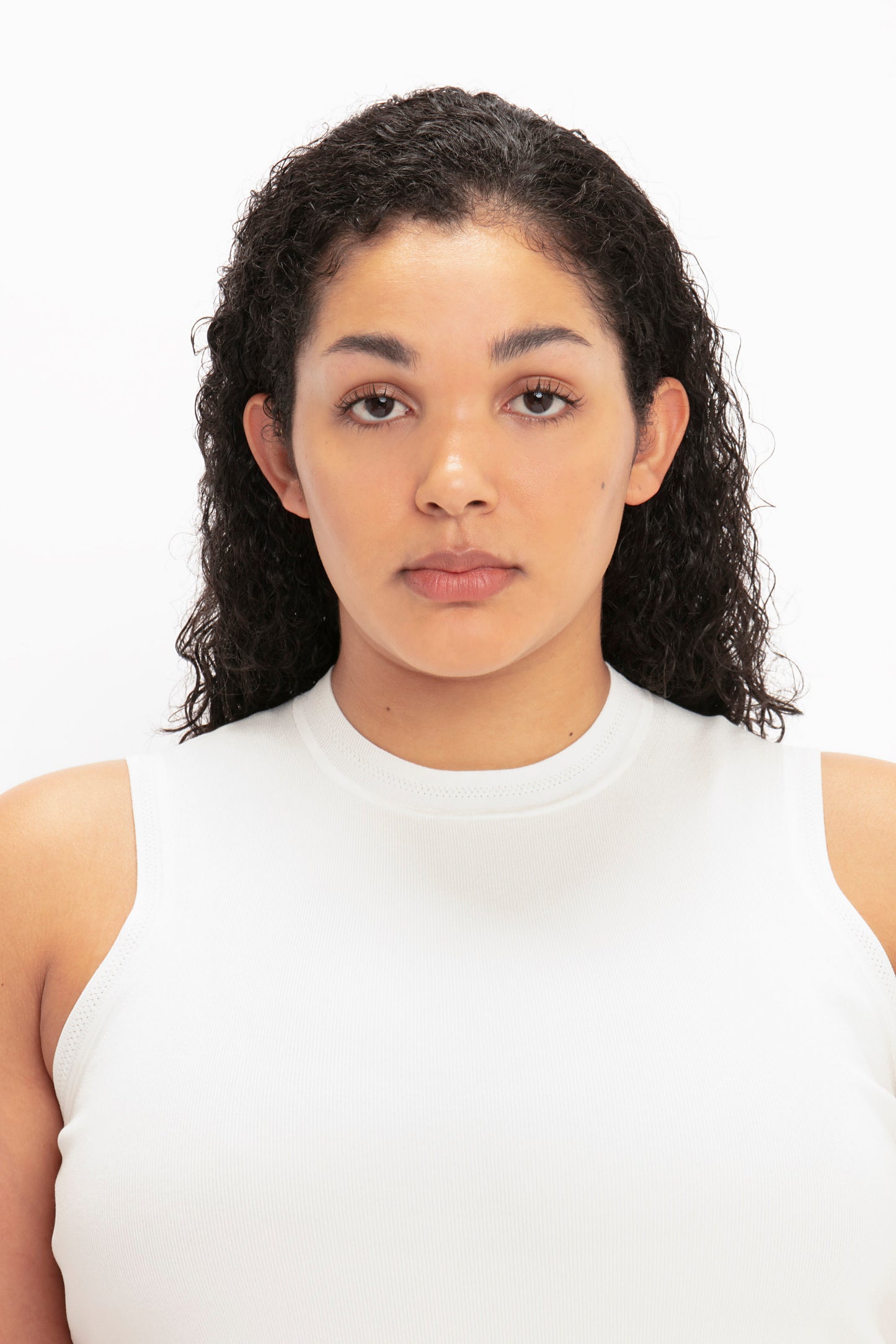 A person with curly hair, wearing a VB Body Mini Dress in White by Victoria Beckham, looking directly at the camera against a plain white background.