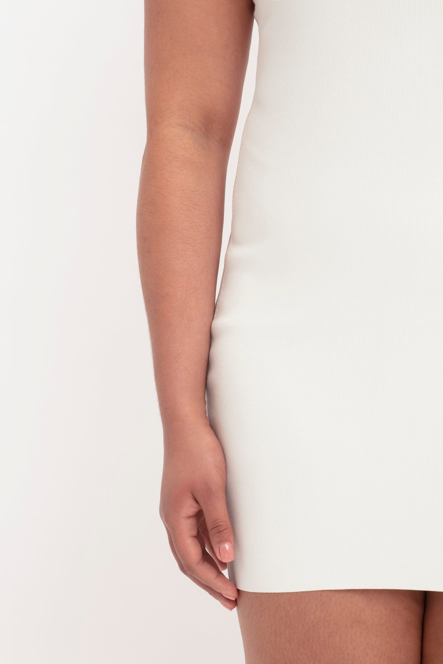 Close-up of a person's left arm and hand resting against their body, standing in the Victoria Beckham VB Body Mini Dress in White.