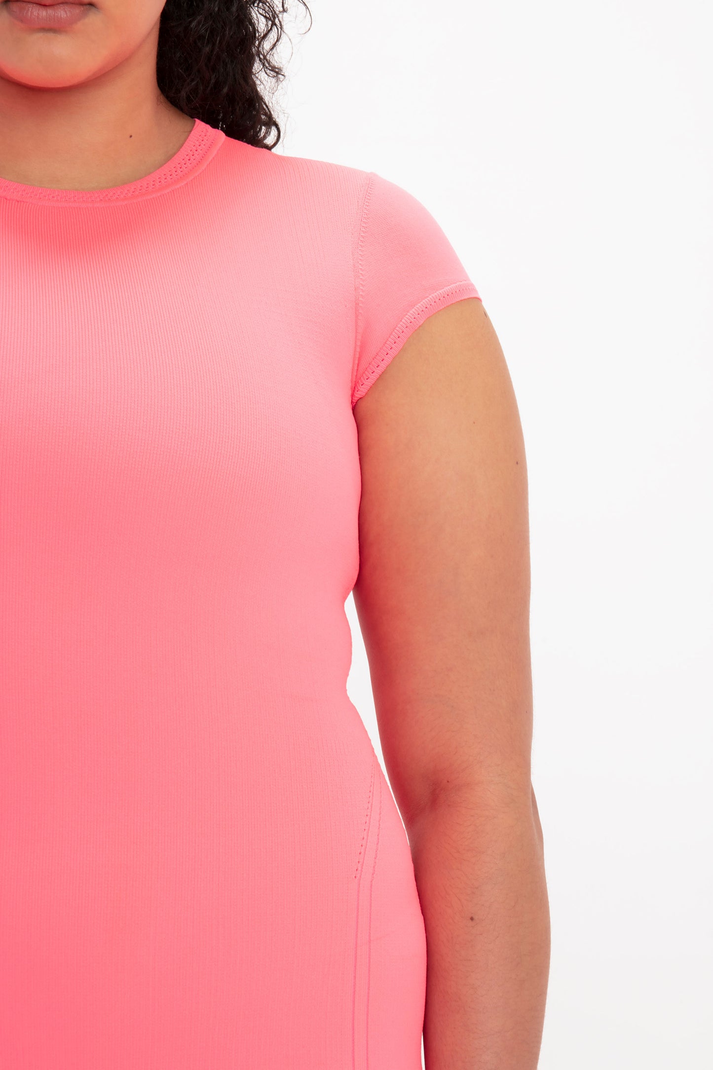 Close-up of a person wearing the Victoria Beckham VB Body Compact Cap Sleeve Mini Dress in Pink, showing their torso and part of their left arm against a plain white background.