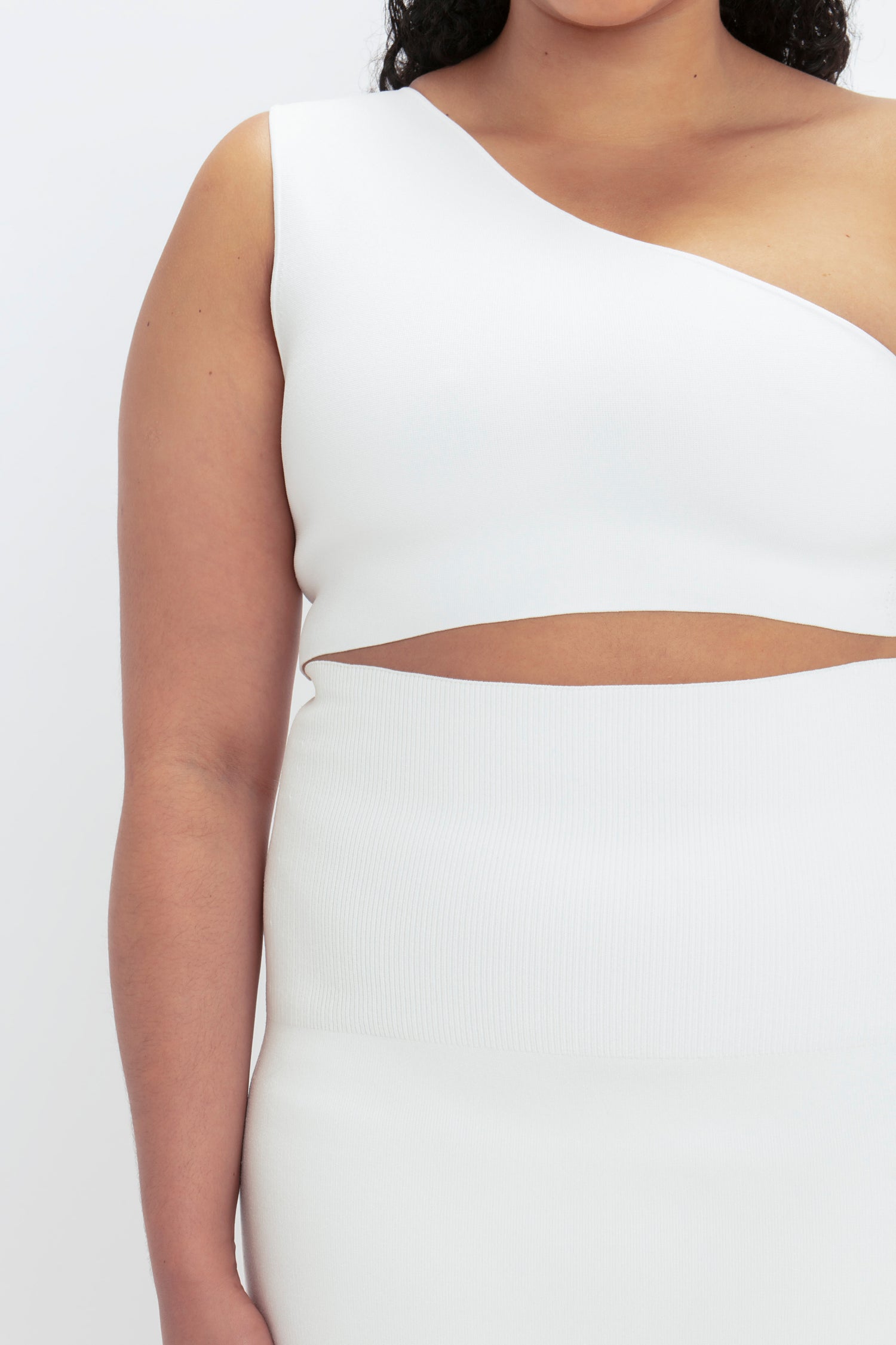 Person wearing the VB Body One Shoulder Crop Top in White by Victoria Beckham, featuring an asymmetrical, sleeveless design with a midriff cutout.