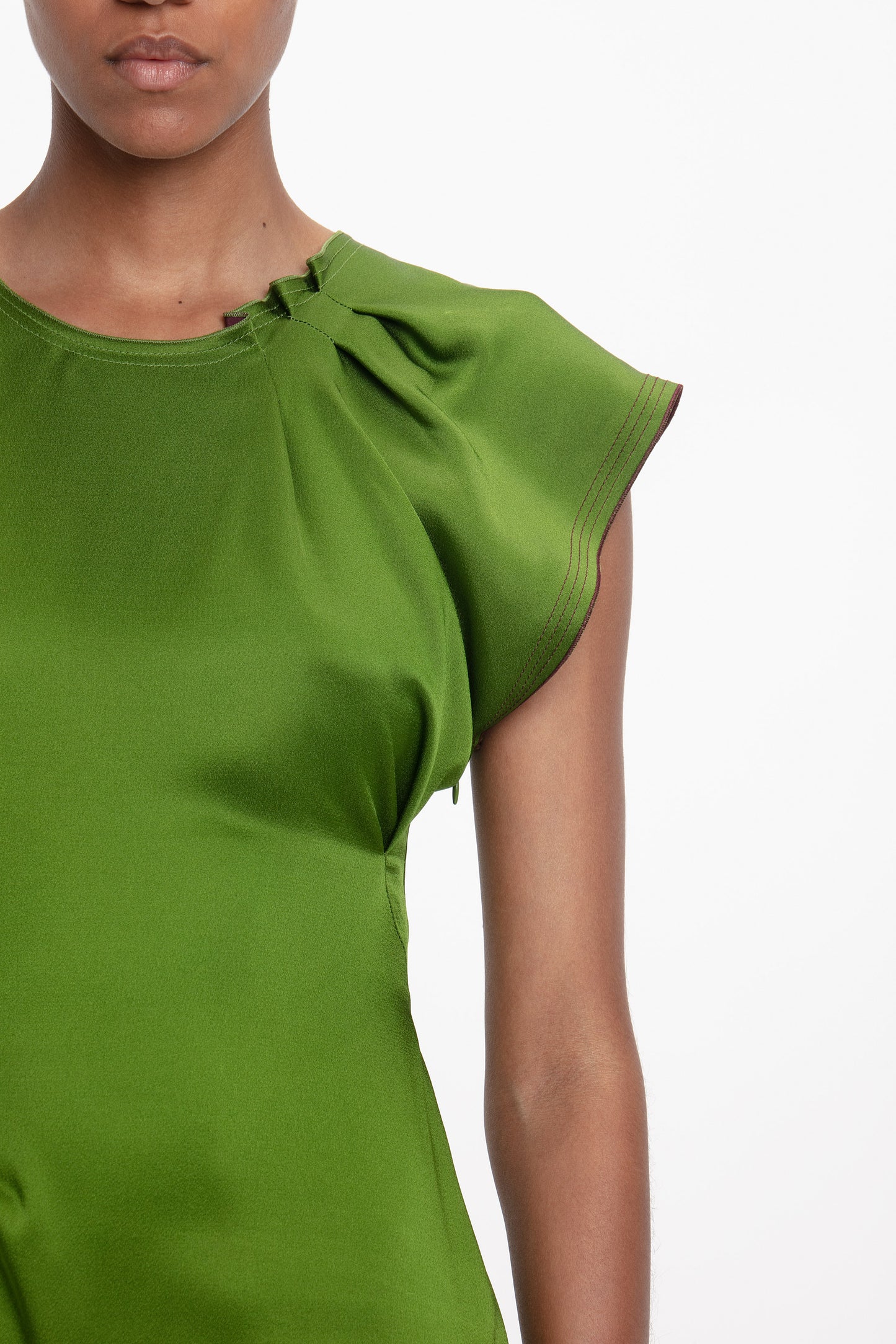 A person stands against a white background, wearing the Victoria Beckham Draped Tuck Detail Midi Dress in algae green, featuring short sleeves and gathered shoulder details.