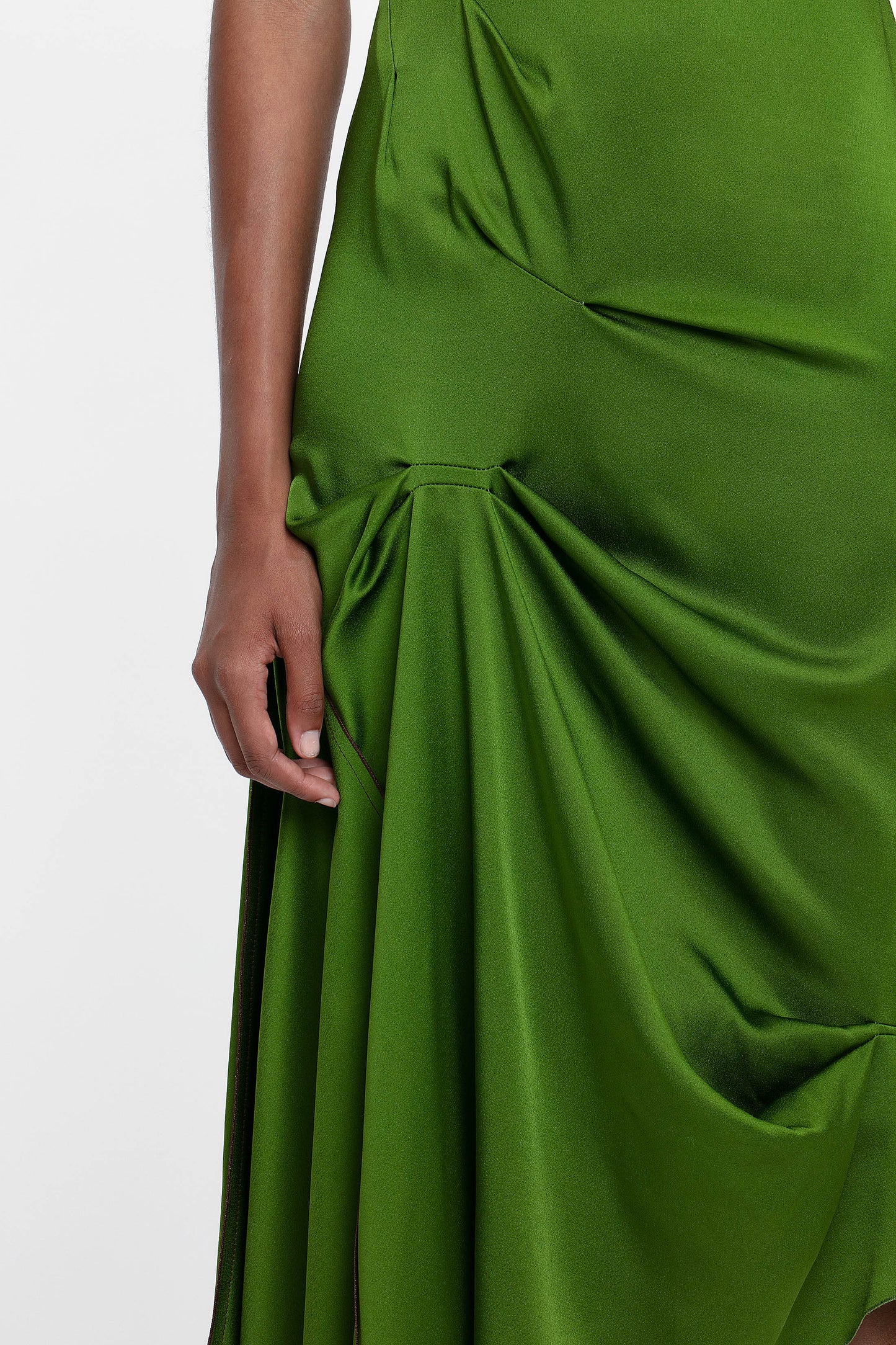 Wearing a Victoria Beckham Draped Tuck Detail Midi Dress in Algae Green, the individual stands gracefully with their hand resting by their side.