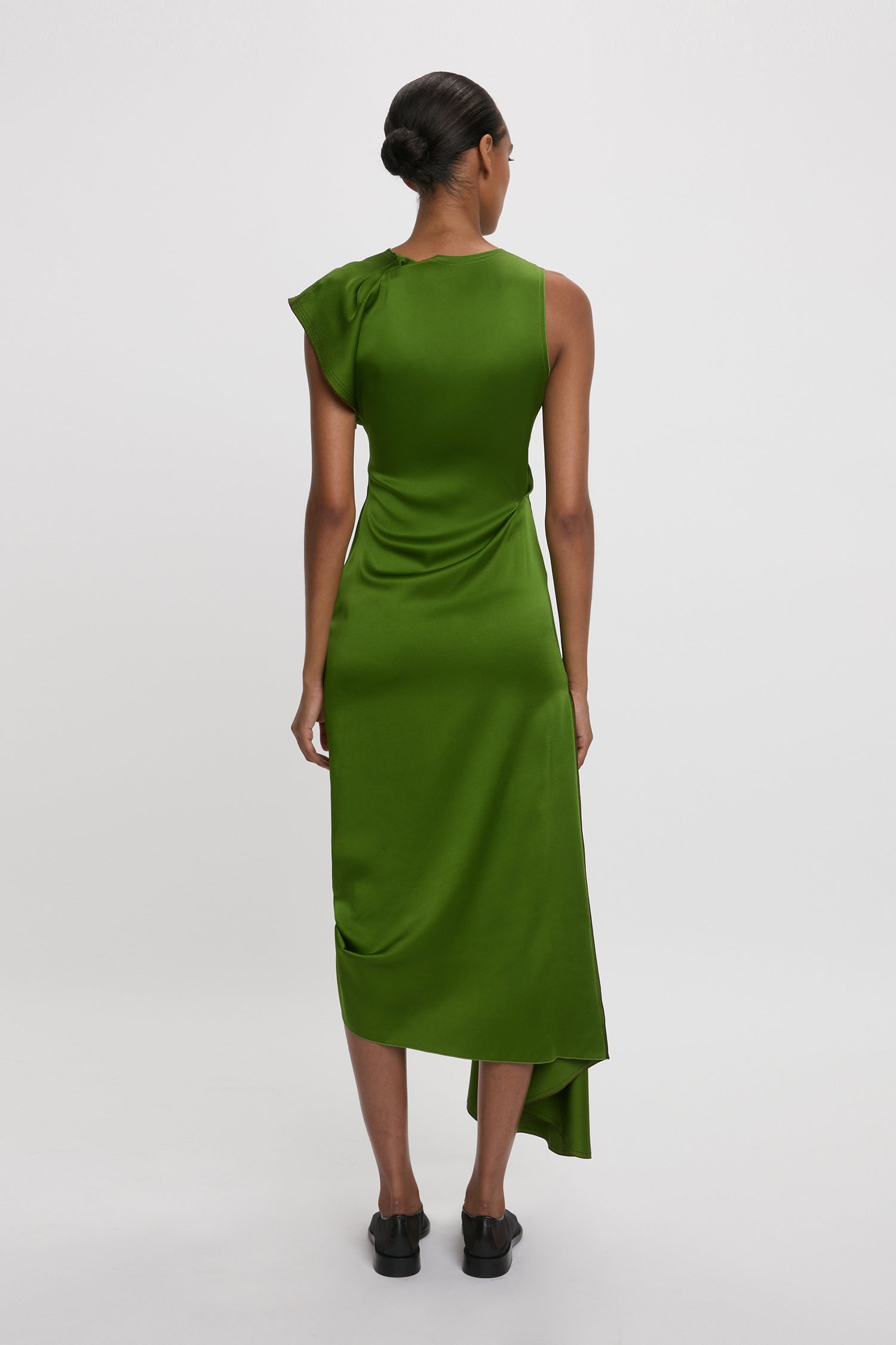 Back view of a person in an Algae Green Draped Tuck Detail Midi Dress with an asymmetrical hem and black shoes, reminiscent of Victoria Beckham's Spring Summer 2025 collection, against a plain white background.