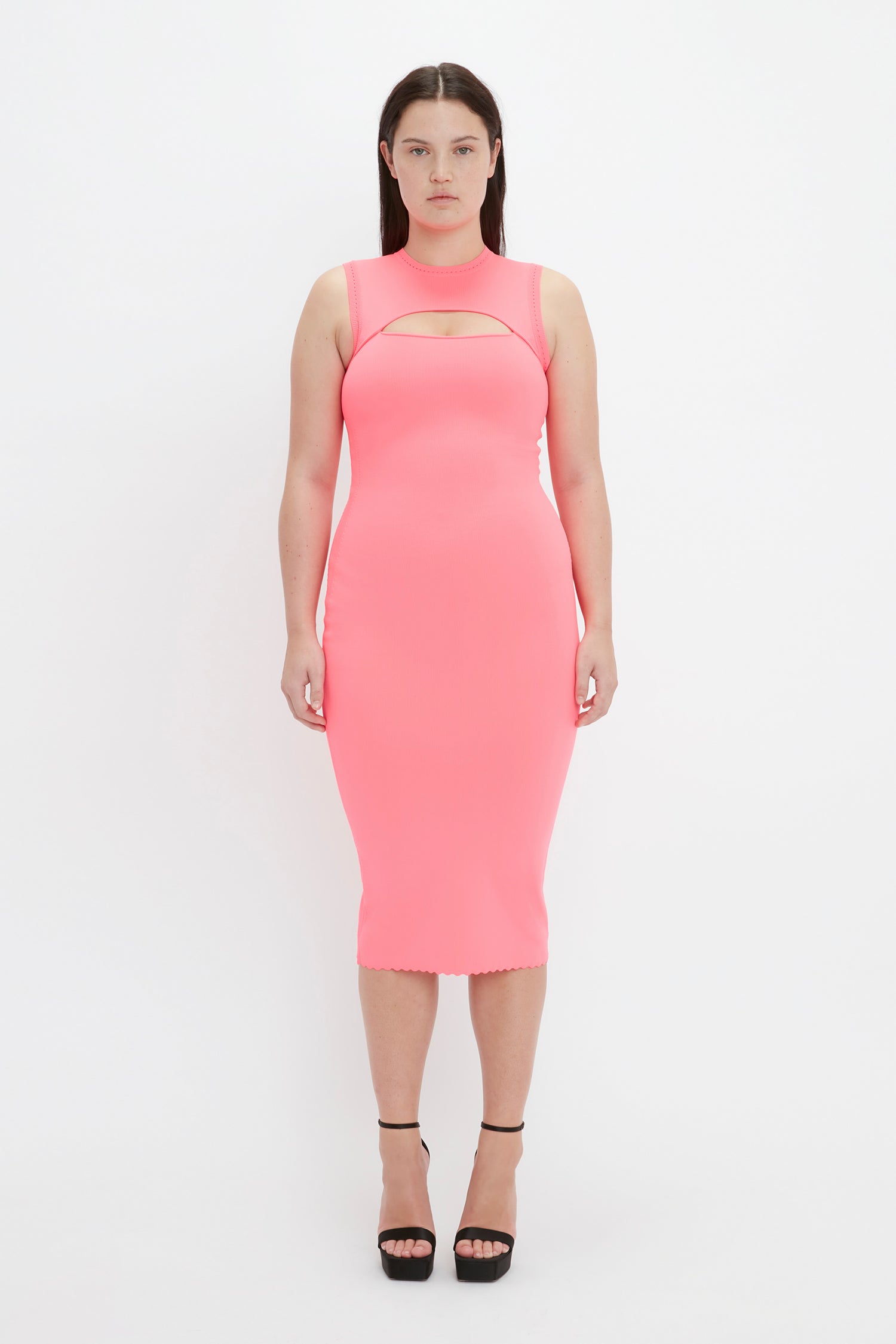 Woman in Victoria Beckham's VB Body Slash Front Midi Dress in pink, standing against a white background and wearing black high-heeled shoes.