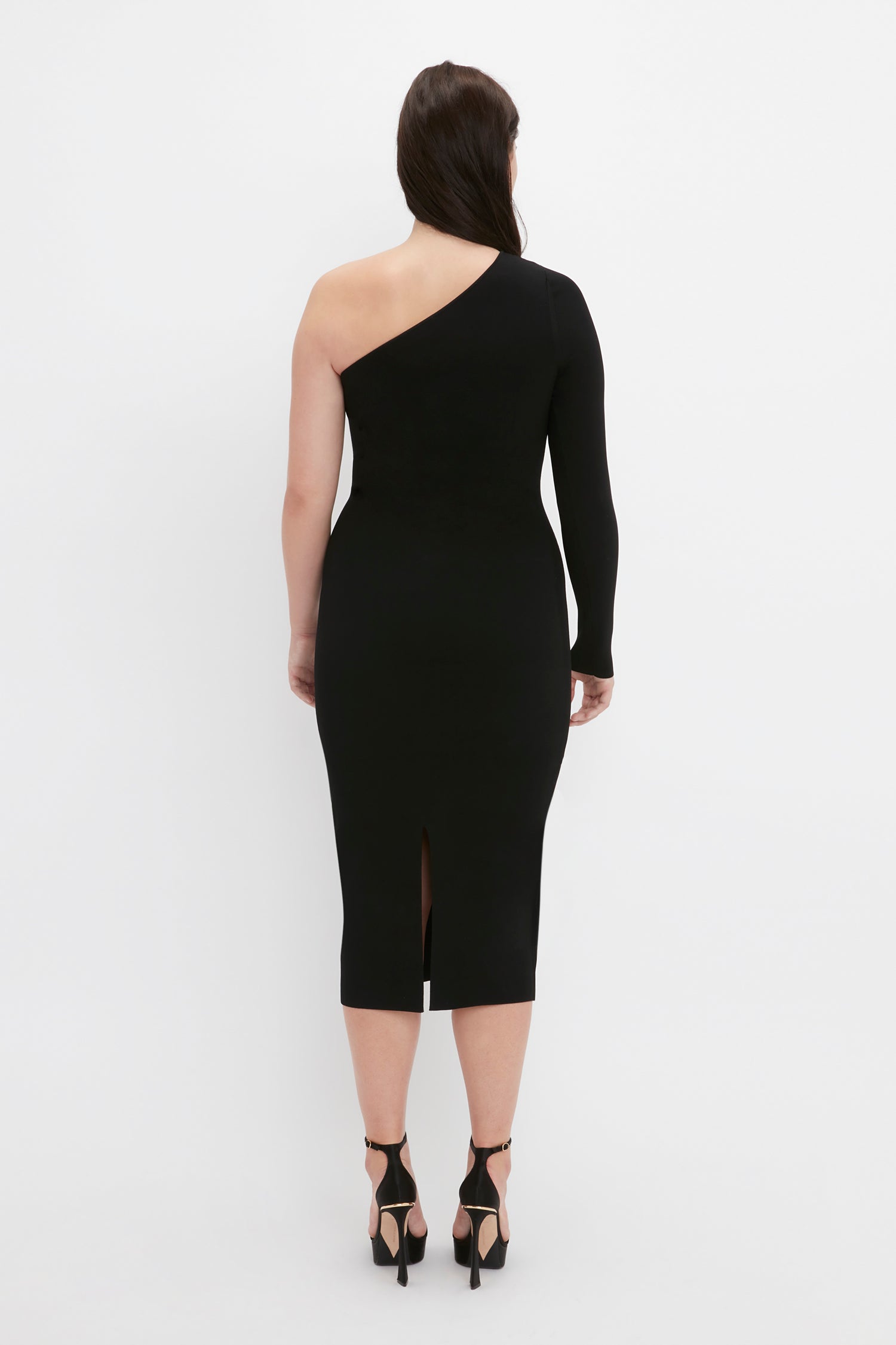 Victoria Beckham VB Body One Shoulder Midi Dress in Black, featuring a slit in the back, worn by a person standing with their back facing the camera.