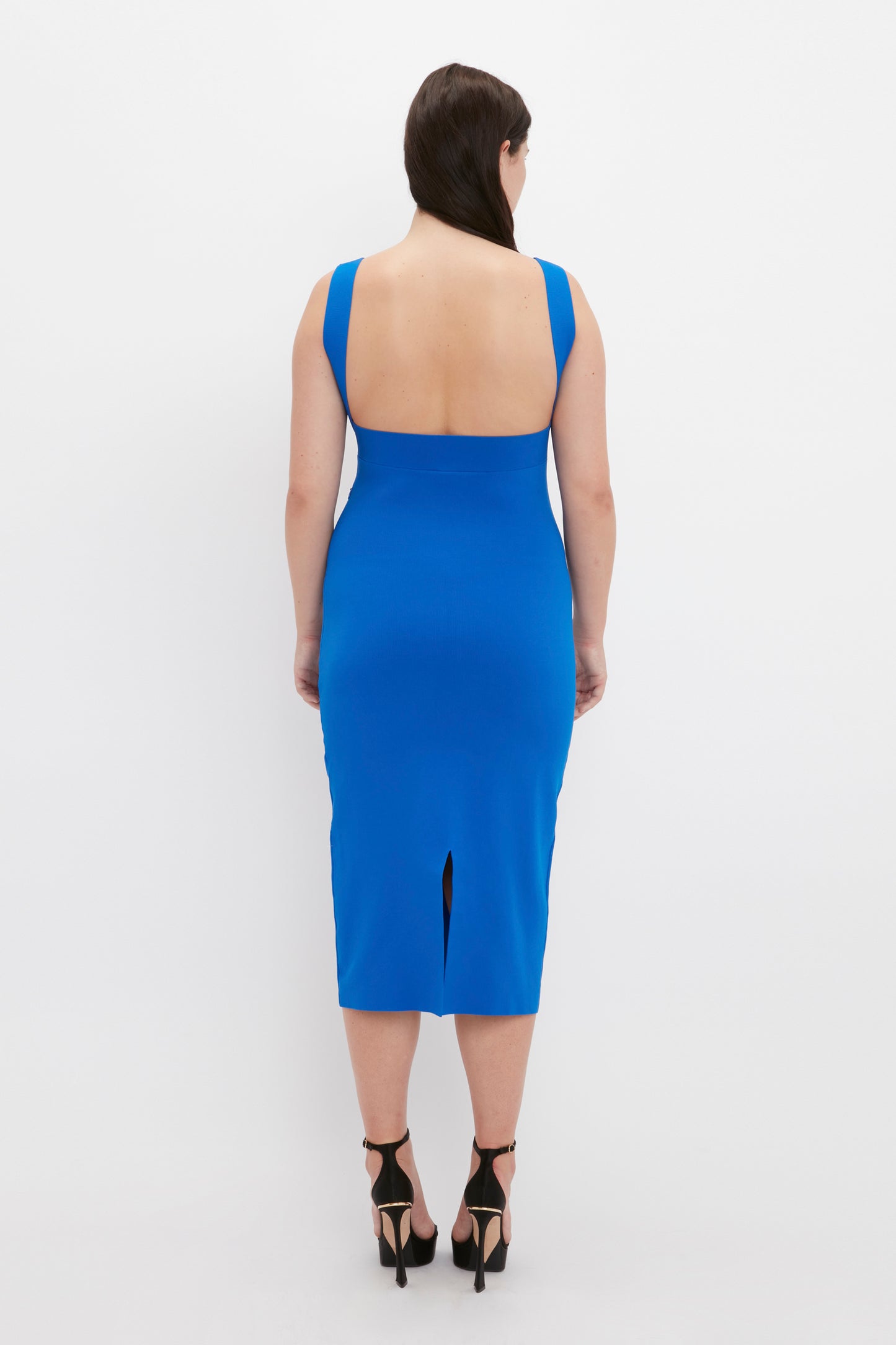 A person wearing the VB Body Cut Out Midi Dress in Cobalt from Victoria Beckham and black high heels, standing with their back facing the camera against a plain white background.