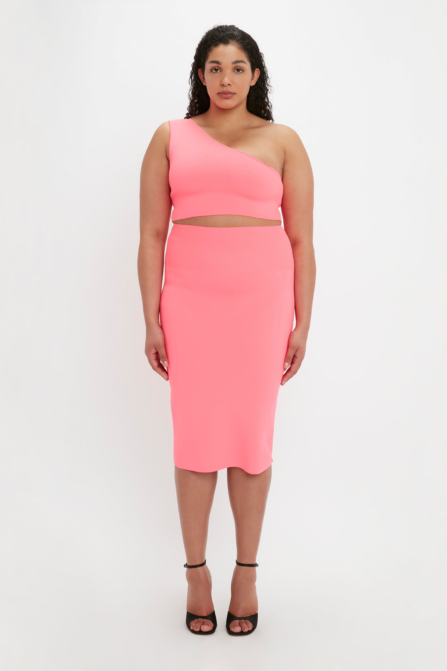 A woman stands against a white background wearing the VB Body One Shoulder Crop Top in Pink by Victoria Beckham.