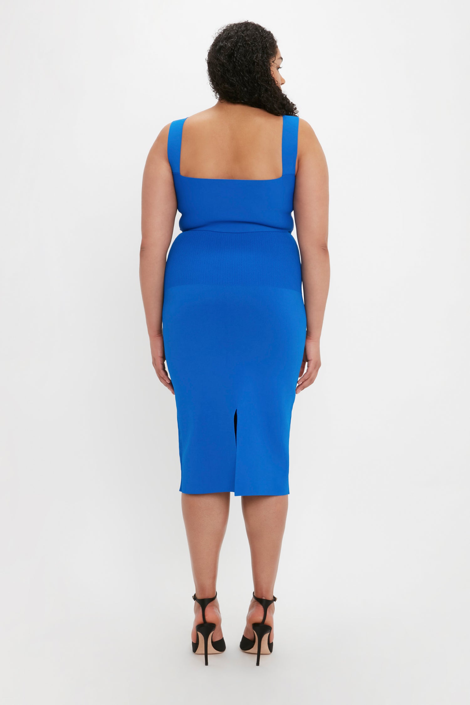 A person with curly hair wearing the VB Body Strap Bandeau Top in Cobalt by Victoria Beckham stands facing away from the camera on a white background.