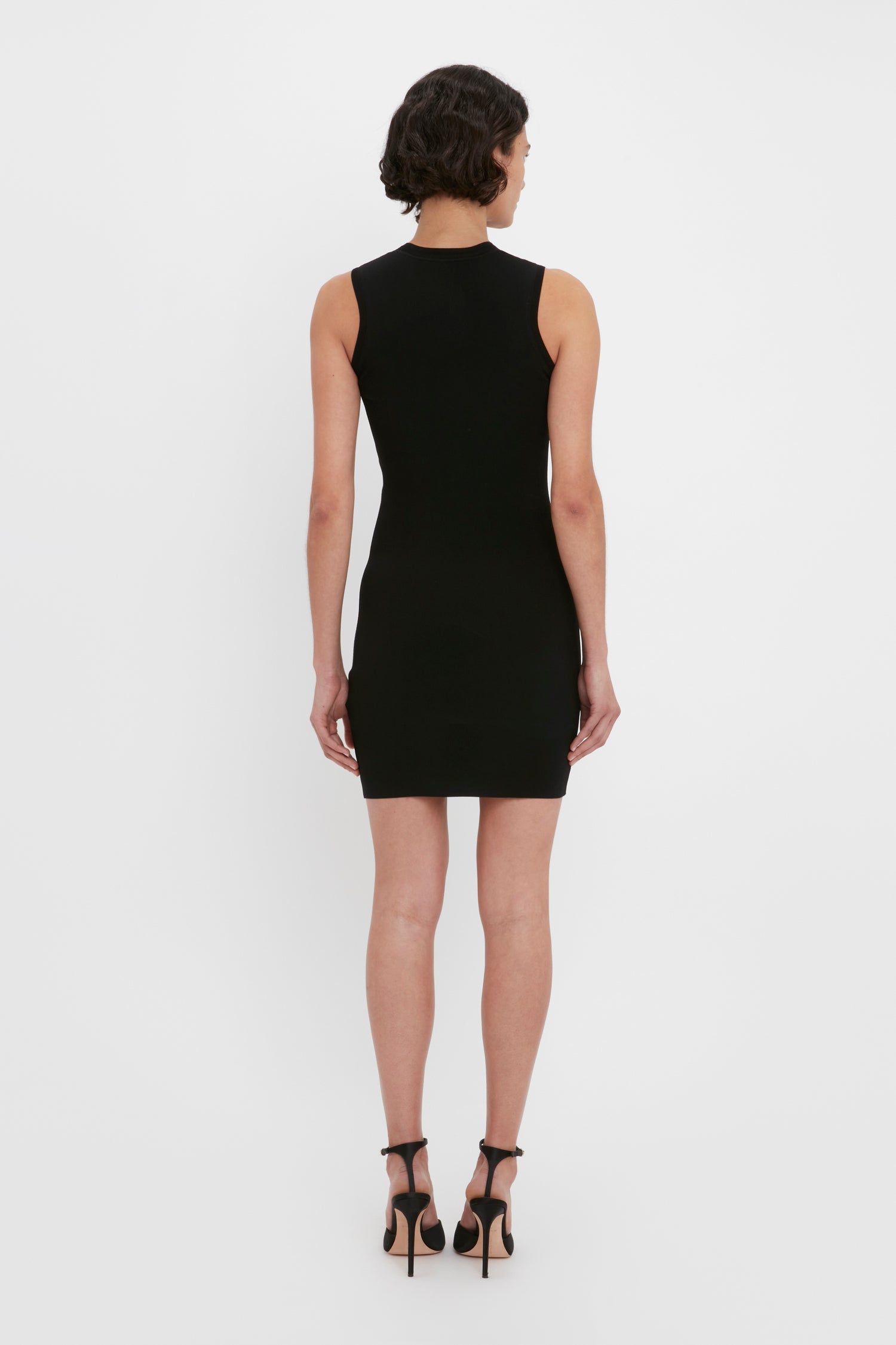 A person wearing the VB Body Mini Dress by Victoria Beckham and black high heels is standing with their back to the camera against a plain white background.