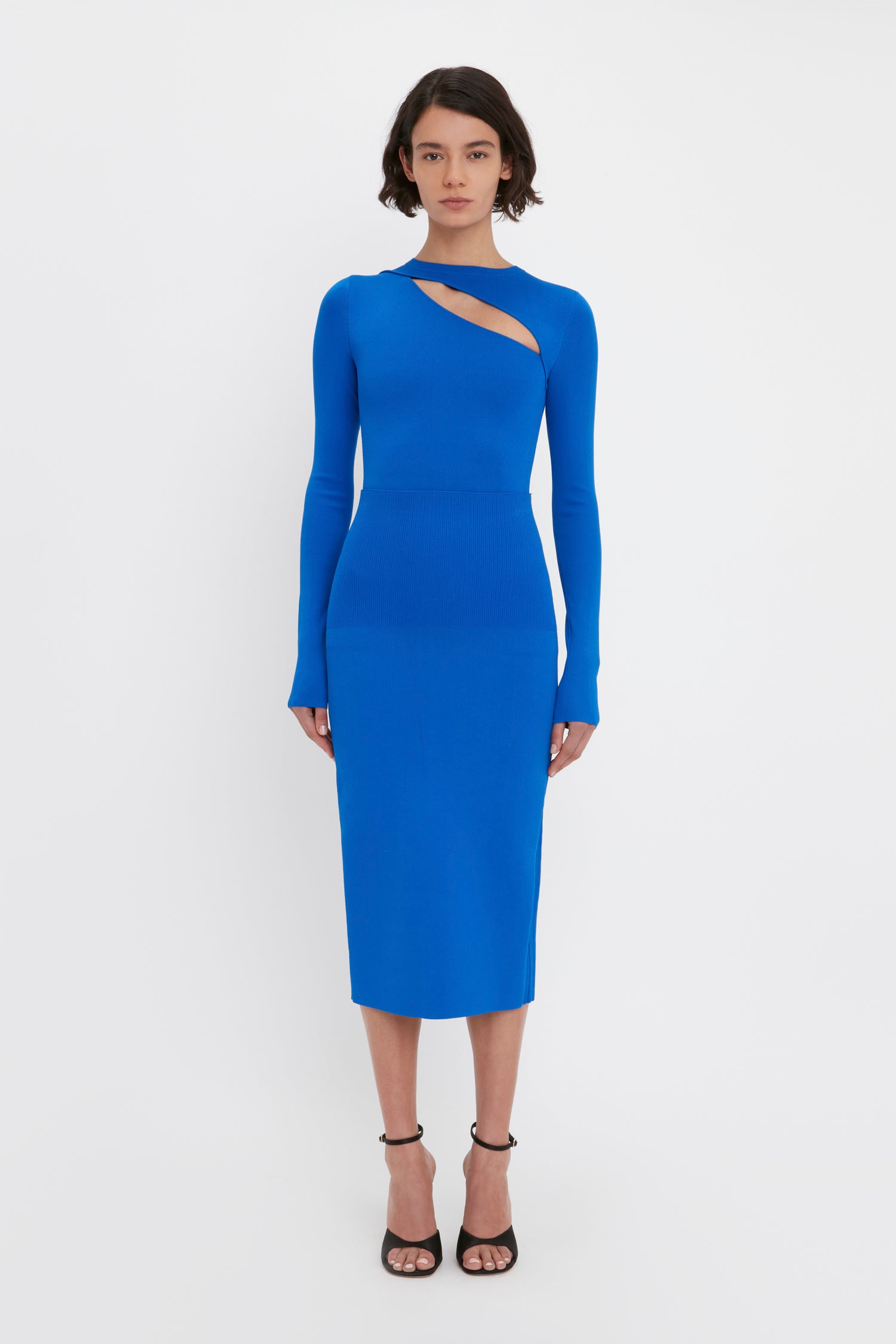 A woman is standing against a white background wearing the VB Body Front Slash Crew Neck Top in Cobalt from Victoria Beckham, paired with black strappy heels.