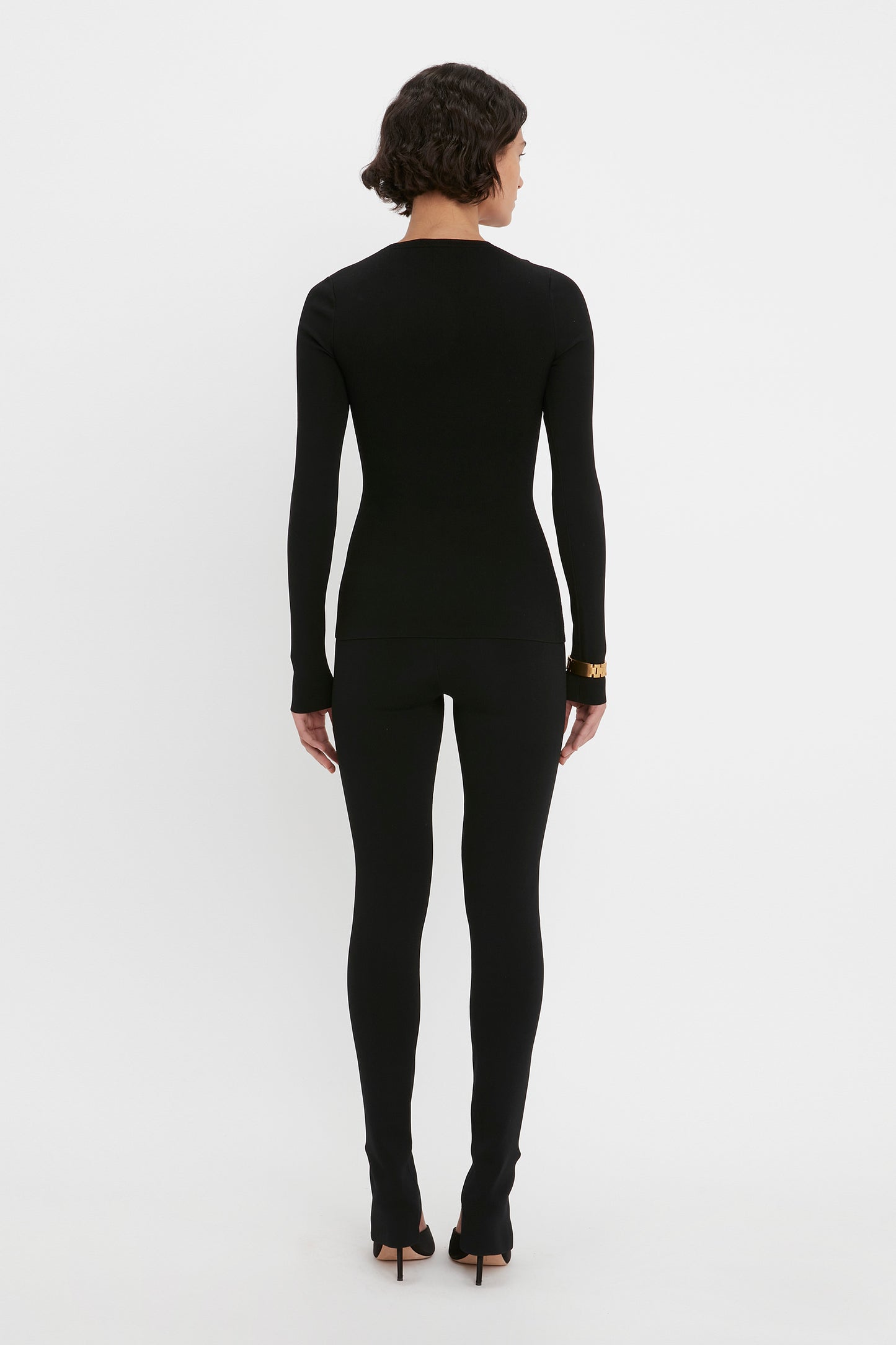 A person dressed in the VB Body Front Slash Crew Neck Top in Black by Victoria Beckham, viewed from behind, standing against a plain white background.