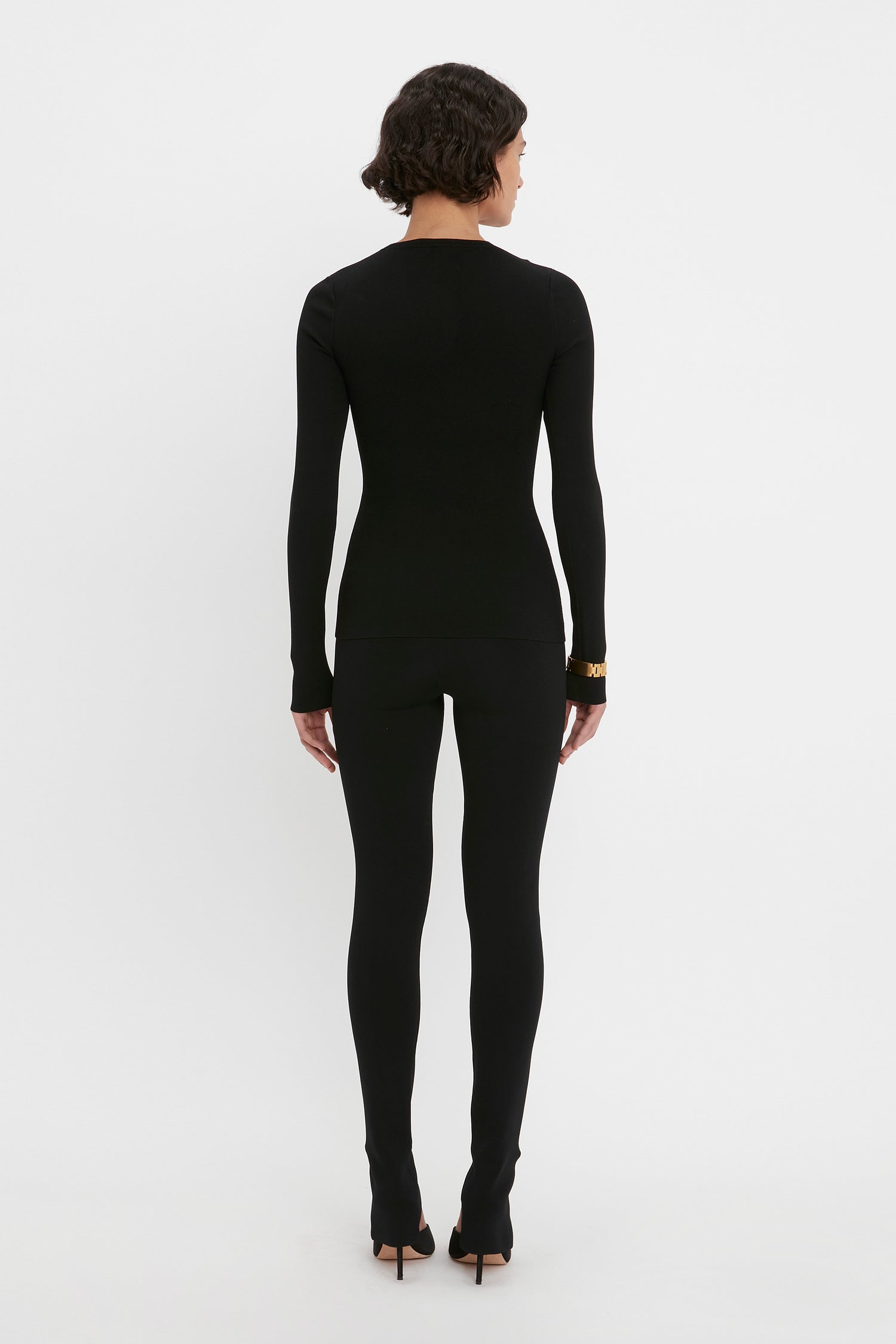 A person dressed in the VB Body Front Slash Crew Neck Top in Black by Victoria Beckham, viewed from behind, standing against a plain white background.