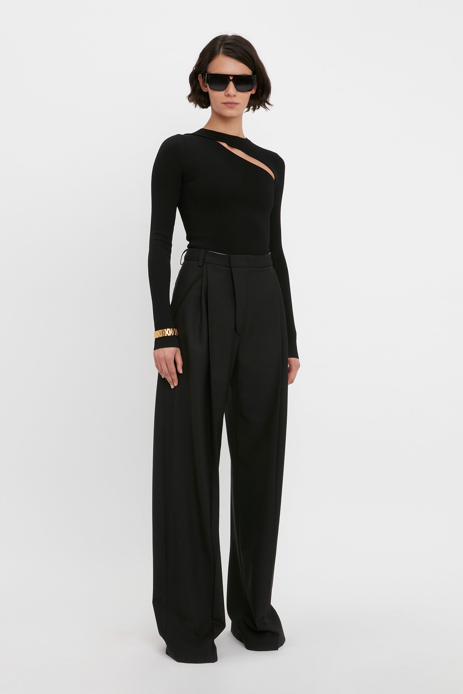 Person wearing the Victoria Beckham VB Body Front Slash Crew Neck Top in Black and wide-leg trousers, accessorized with sunglasses and a bracelet.